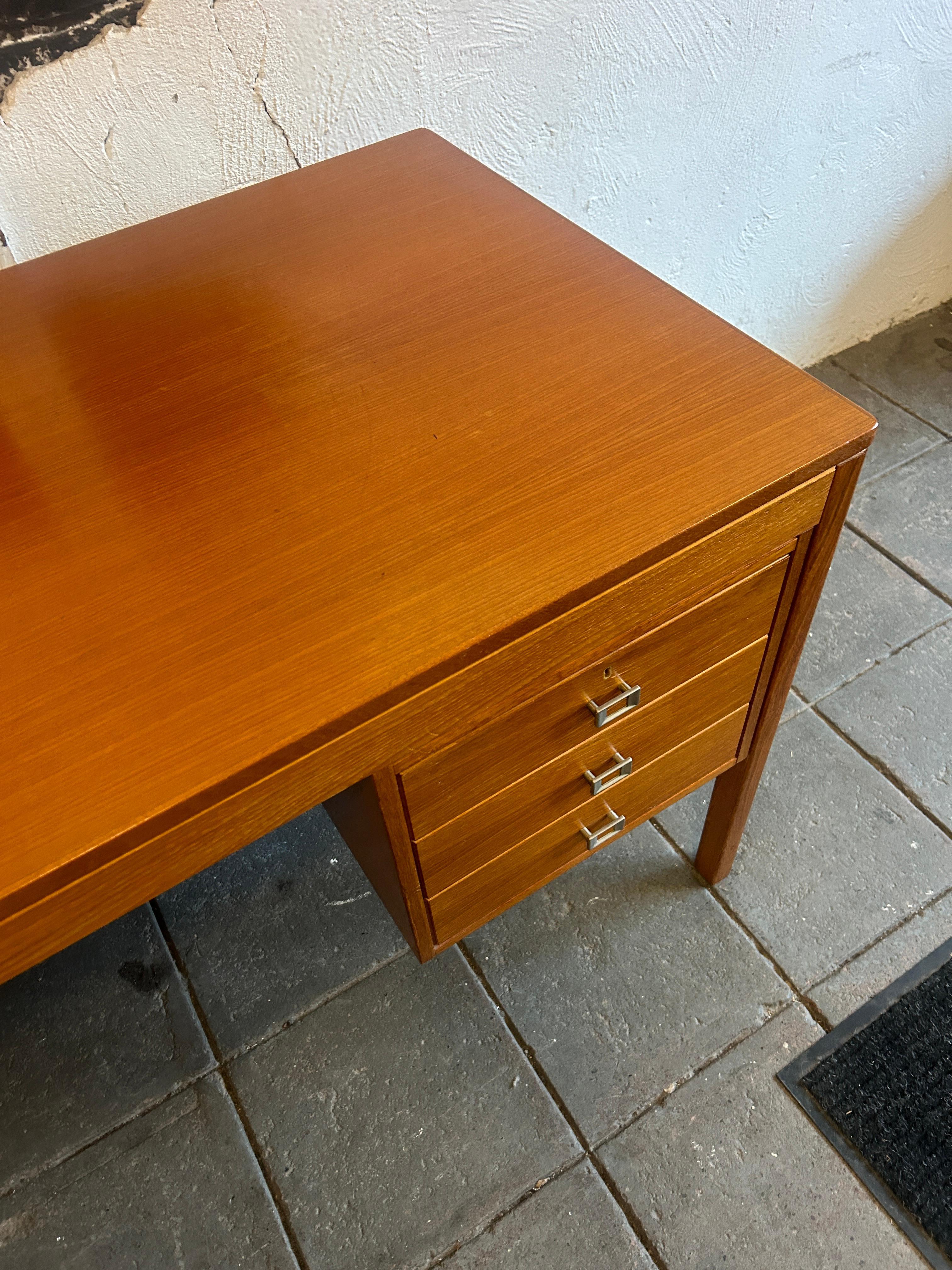 Mid century Danish modern teak desk with nickel handles with key. Kneehole desk with (3) slim drawers on the left and (1) large file drawer on the right. Nice nickel pulls and key. Top drawer on left and large drawer on right locks. Nice teak wood