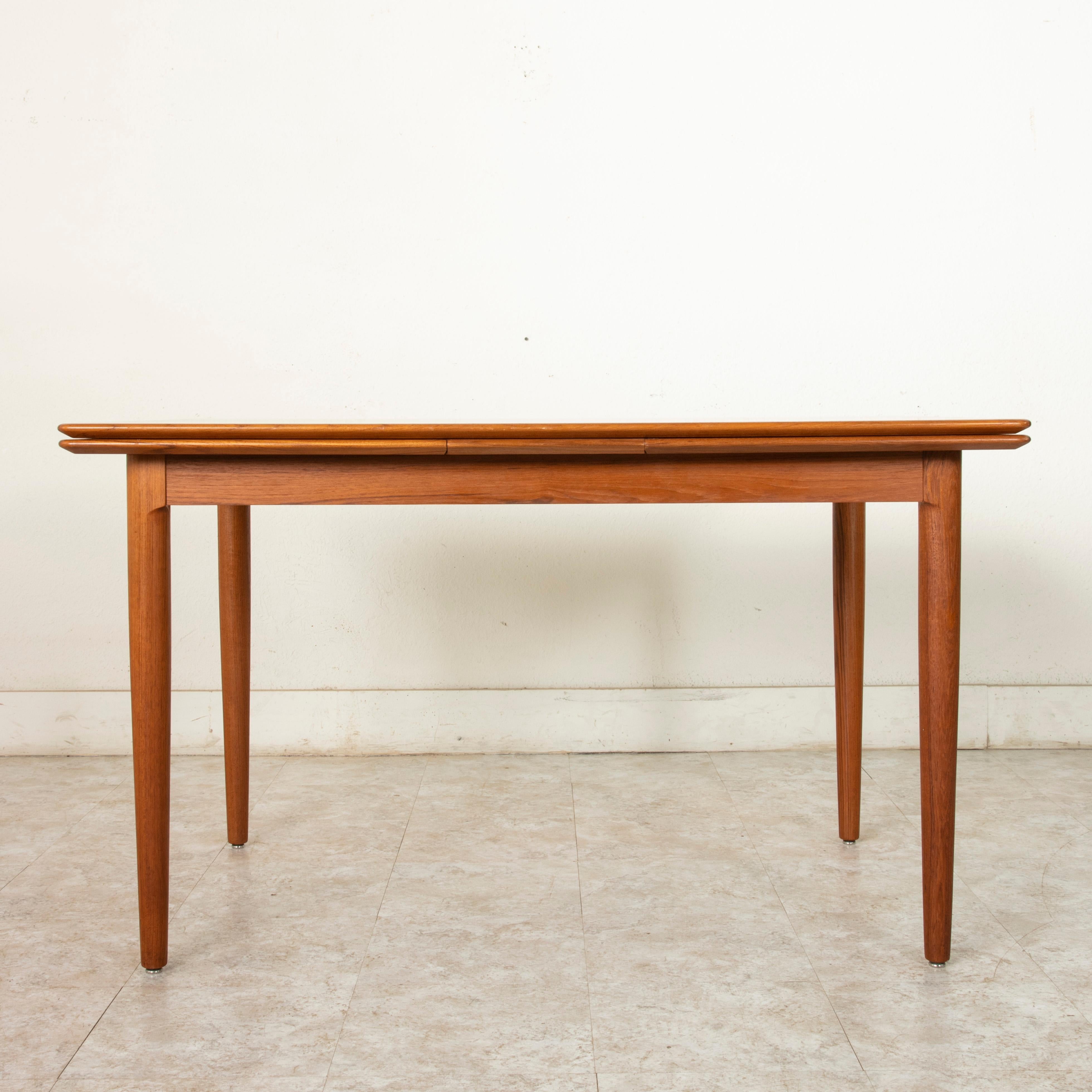 This Mid-Century Modern Danish dining table constructed of teak wood features a nearly 50 inch long by 34 inch wide top that rests on sleek tapered legs. Draw leaves add an additional 19.5 inches to each end allowing for a total length of 88.5