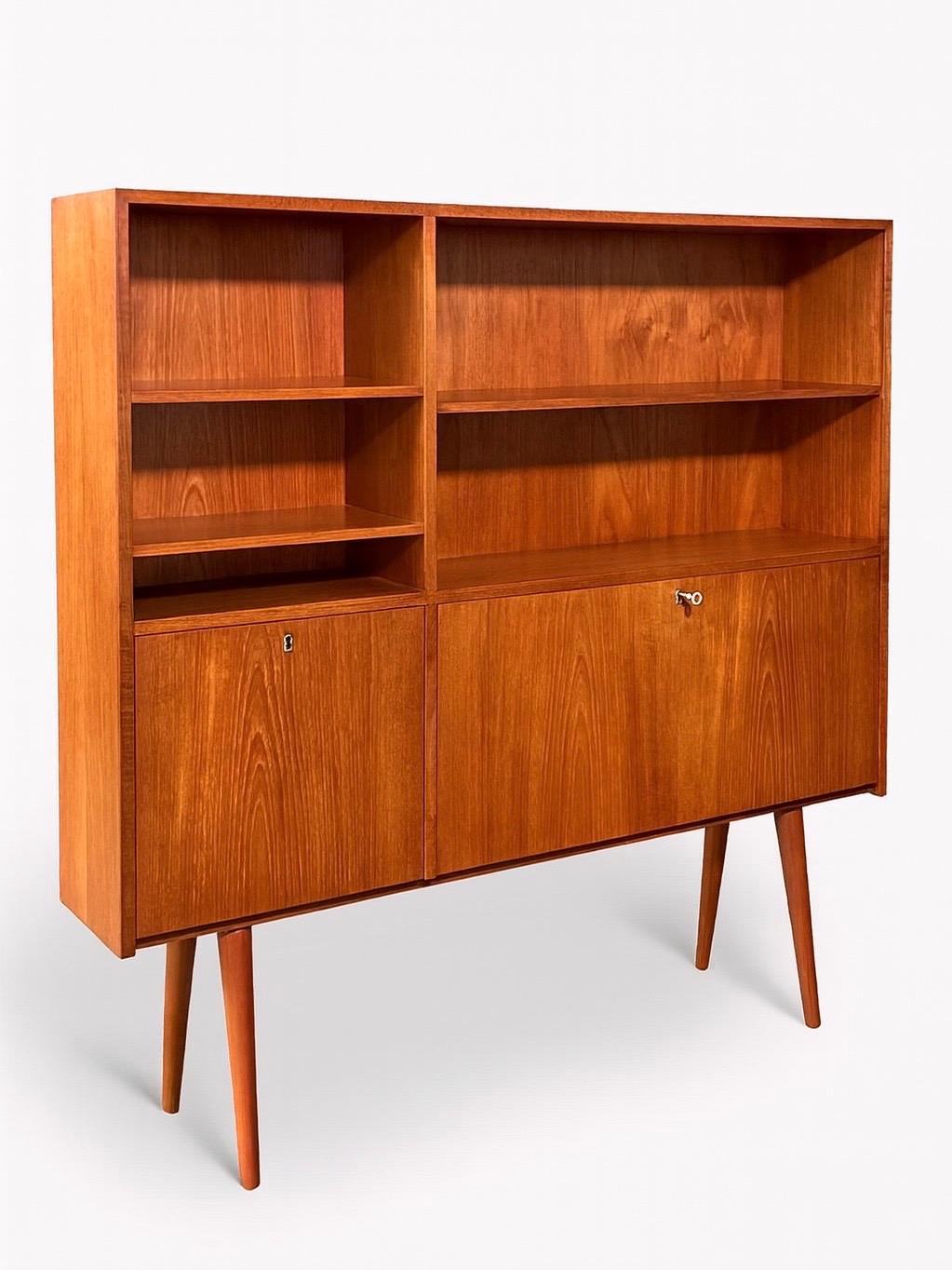 Condizioni: Condizioni originali d'epoca
Materiali: Teak, chiave scheletrica originale in ottone 
Stile: Moderno danese 

Questa libreria a ribalta in teak Danish Modern, realizzata negli anni '60, è un bellissimo esempio di funzionalità e design di
