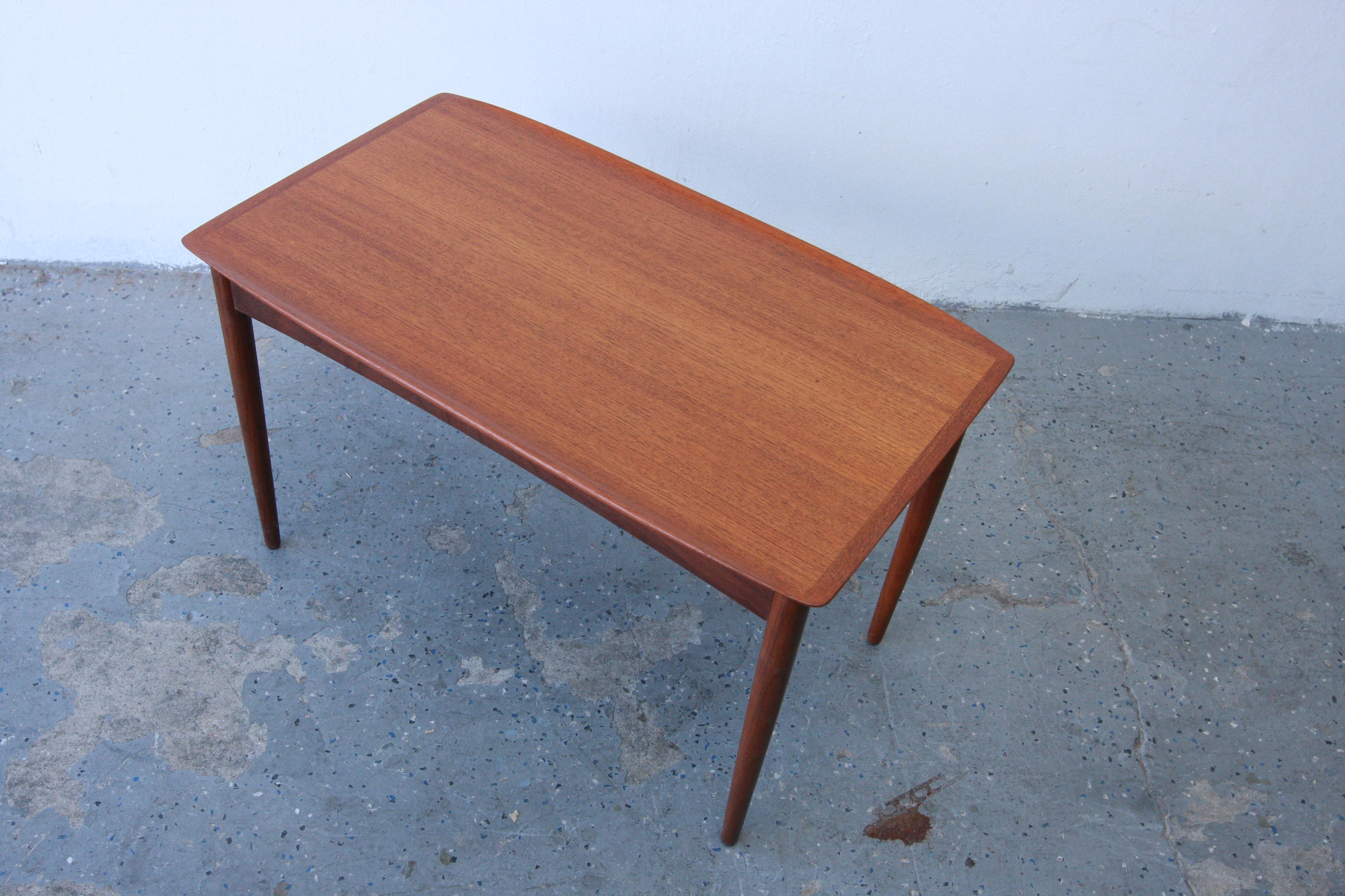 Spectacular 1960s Danish Modern teak side table by Mobelintarsia from Denmark. Features a rectangle shaped top in beautifully grained teak with carved lip edges and the sculpted edges are open at the corners. The table stands on four round tapered