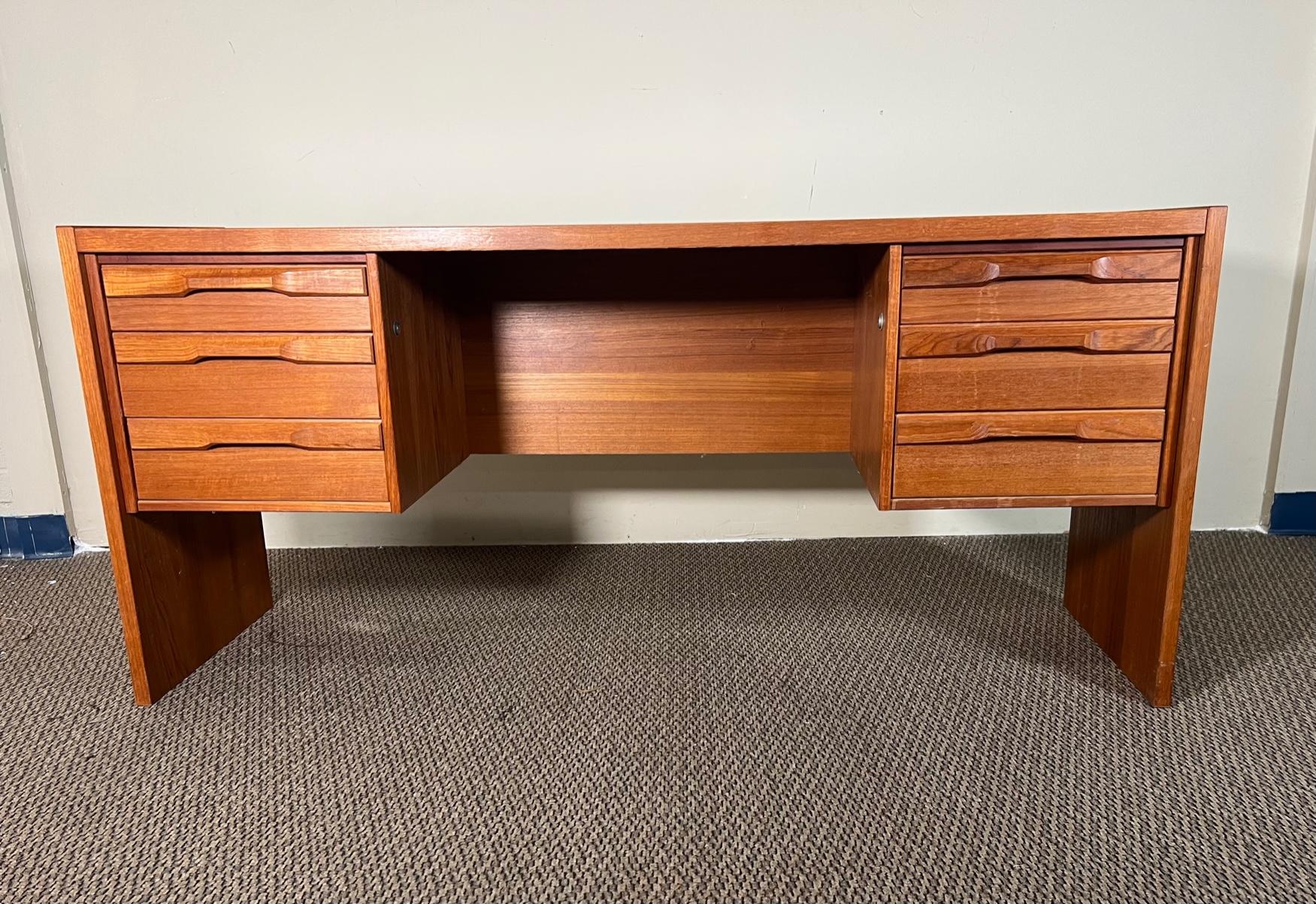Danish teak veneer desk by Denka. Original label on outside of right top drawer. Free standing with finished back. Beautiful sculpted teak handles.
Very good condition overall. Some marks and scratches on the top. All drawers glide well. Some stains