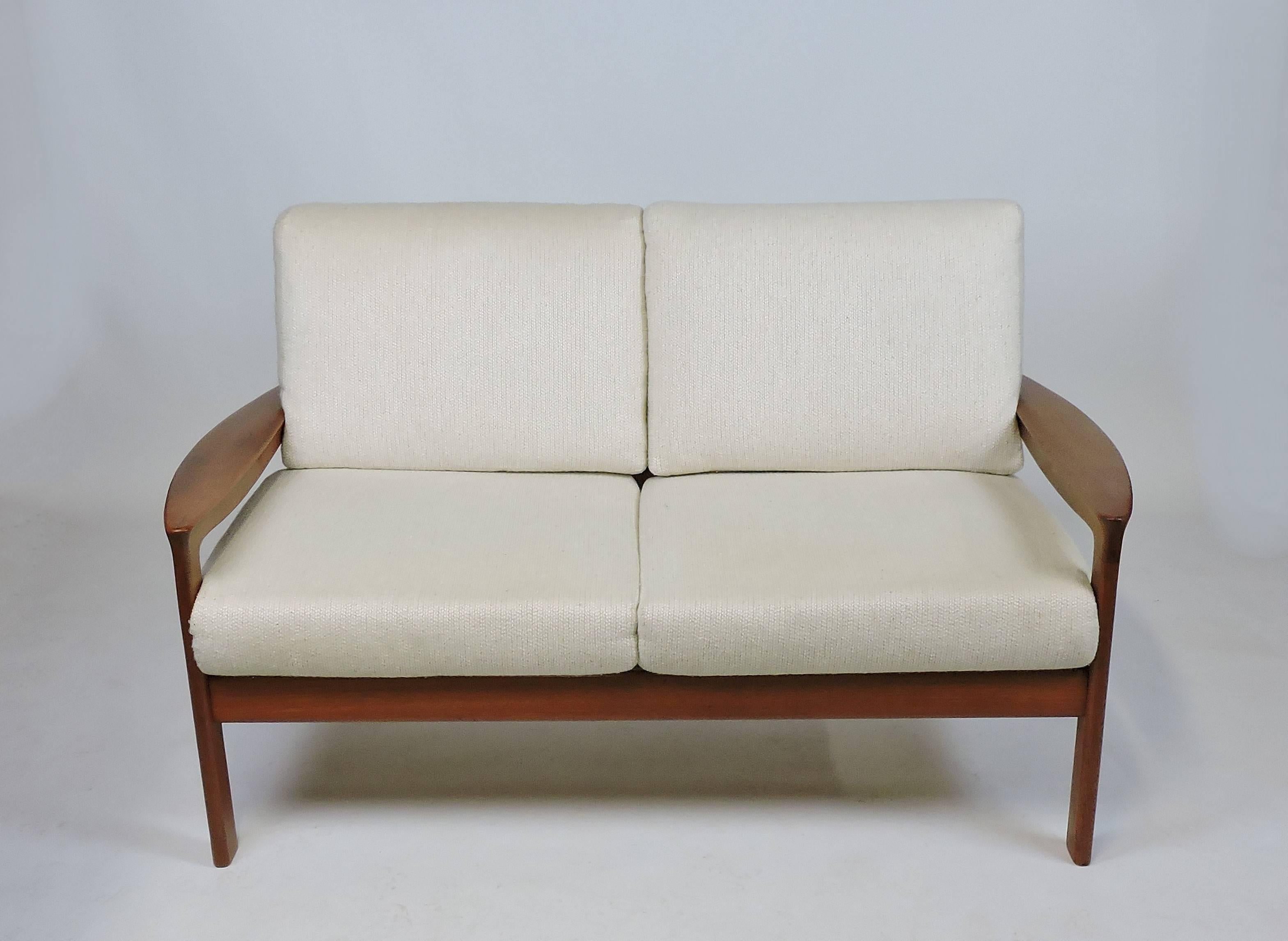 Beautiful and comfortable loveseat made by Komfort of Denmark. It has great craftsmanship with a sculpted solid teak frame with paddle arms, and a slat back. The zippered cushions have the original off-white textured upholstery. 
Unmarked. We also