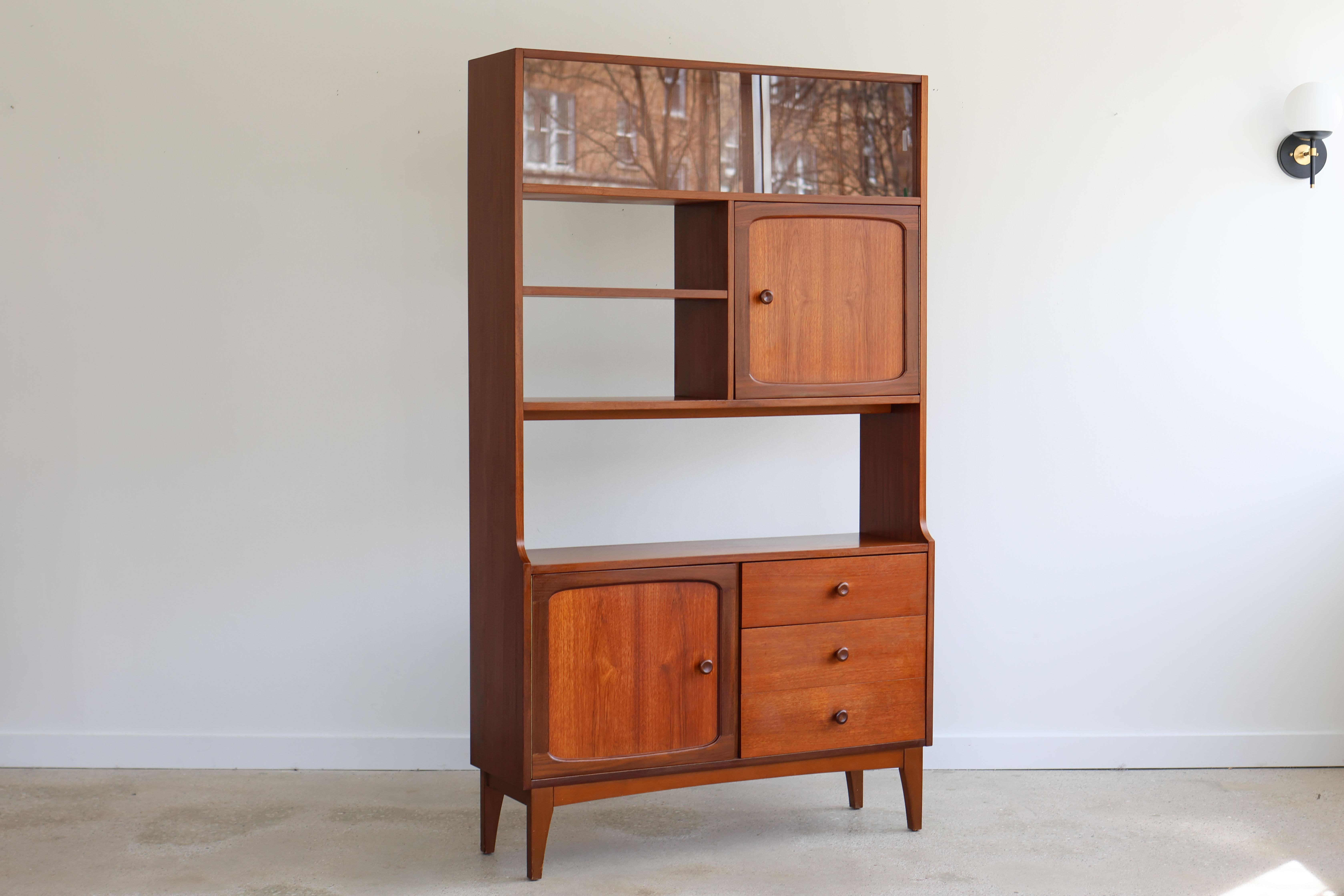 Mid-Century Danish Modern teak shelving unit.
Room divider by Stonehill, made in the UK, 1960s.
One piece narrow unit with finished back.
Two cabinets and three drawers.
Round wooden knobs.
Sliding glass panels on the top for enclosed display