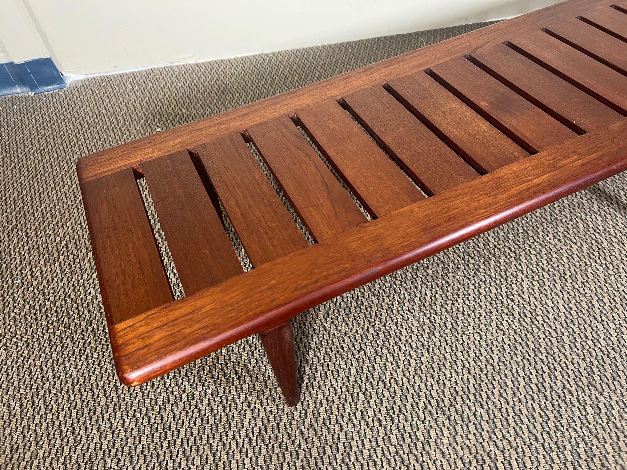 Superb extra long slat bench made of solid teak. Model JH-574 designed by Hans J. Wegner for cabinetmaker Johannes Hansen of Denmark. Dating back to the sixties. The bench is supported by six strong tapered legs. A beautiful example of minimalist