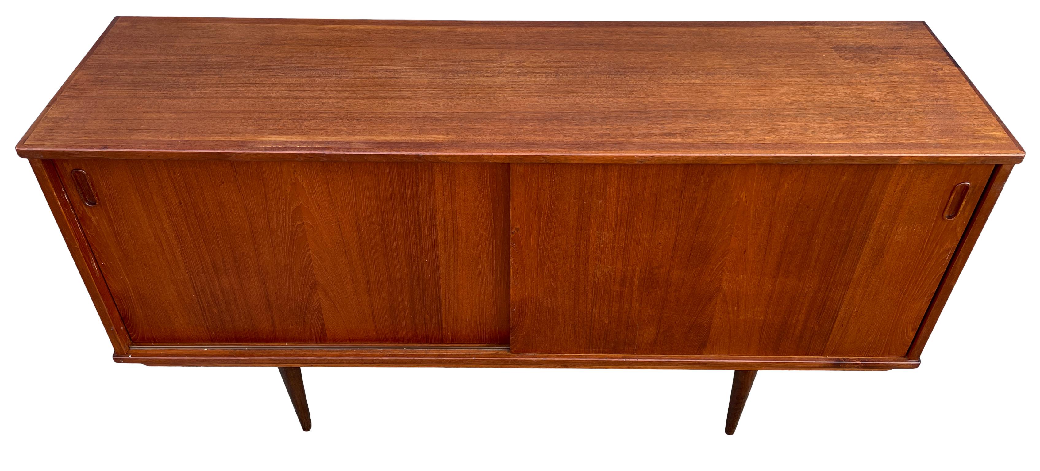 Mid century Danish modern teak sliding door credenza by Dyrlund - Has 2 front sliding doors with carved teak handles. Has 2 adjustable shelves w/pins in each section also has 1 narrow felt covered drawer on the right top of inside the credenza.
