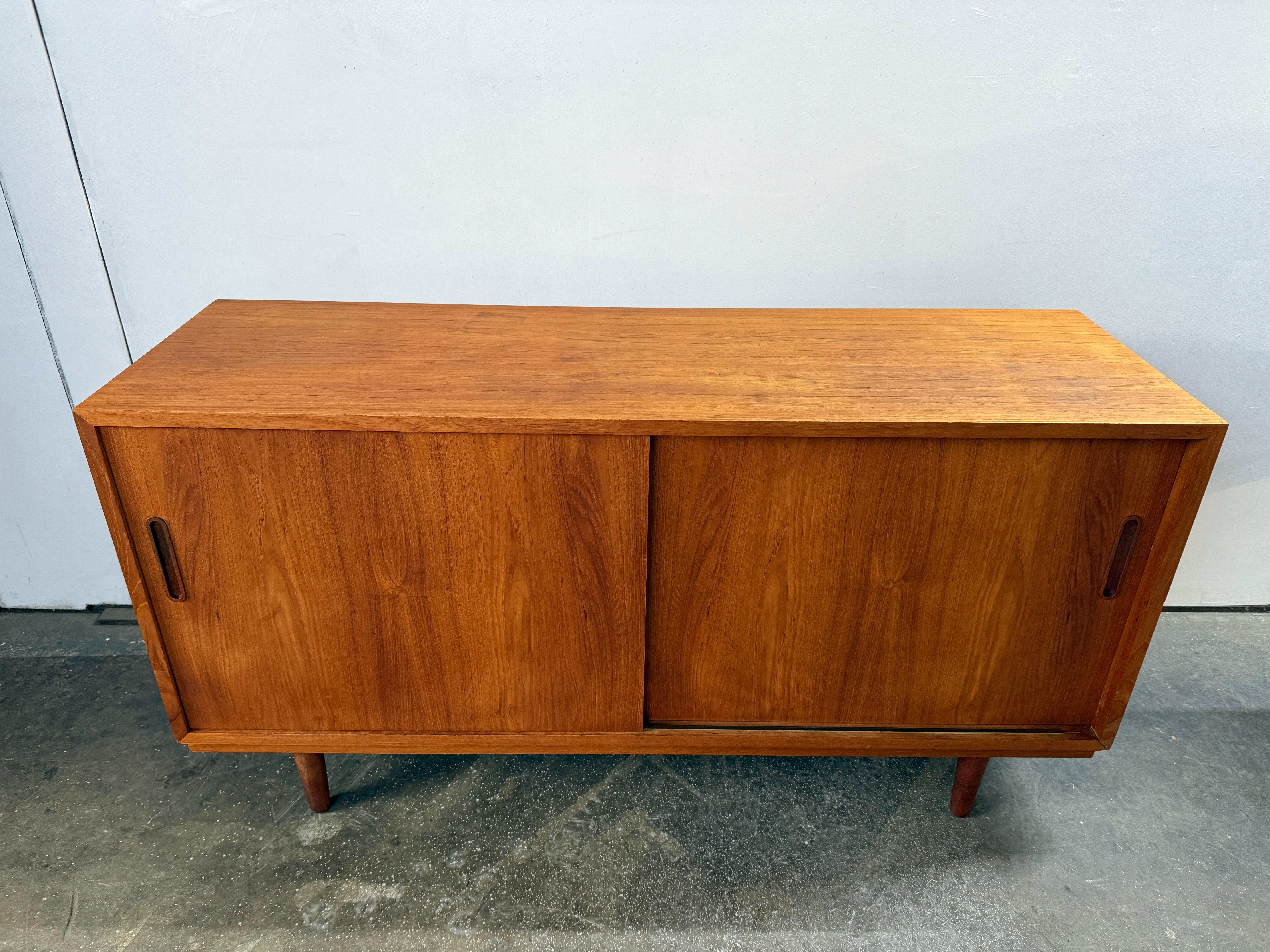 Mid century Danish modern teak sliding door credenza. Has 2 front sliding doors with rounded carved teak handles. Has 2 adjustable or removable shelves w/pins. Labeled Danish Control inside. Good excellent condition inside and out. Sits on 4 solid