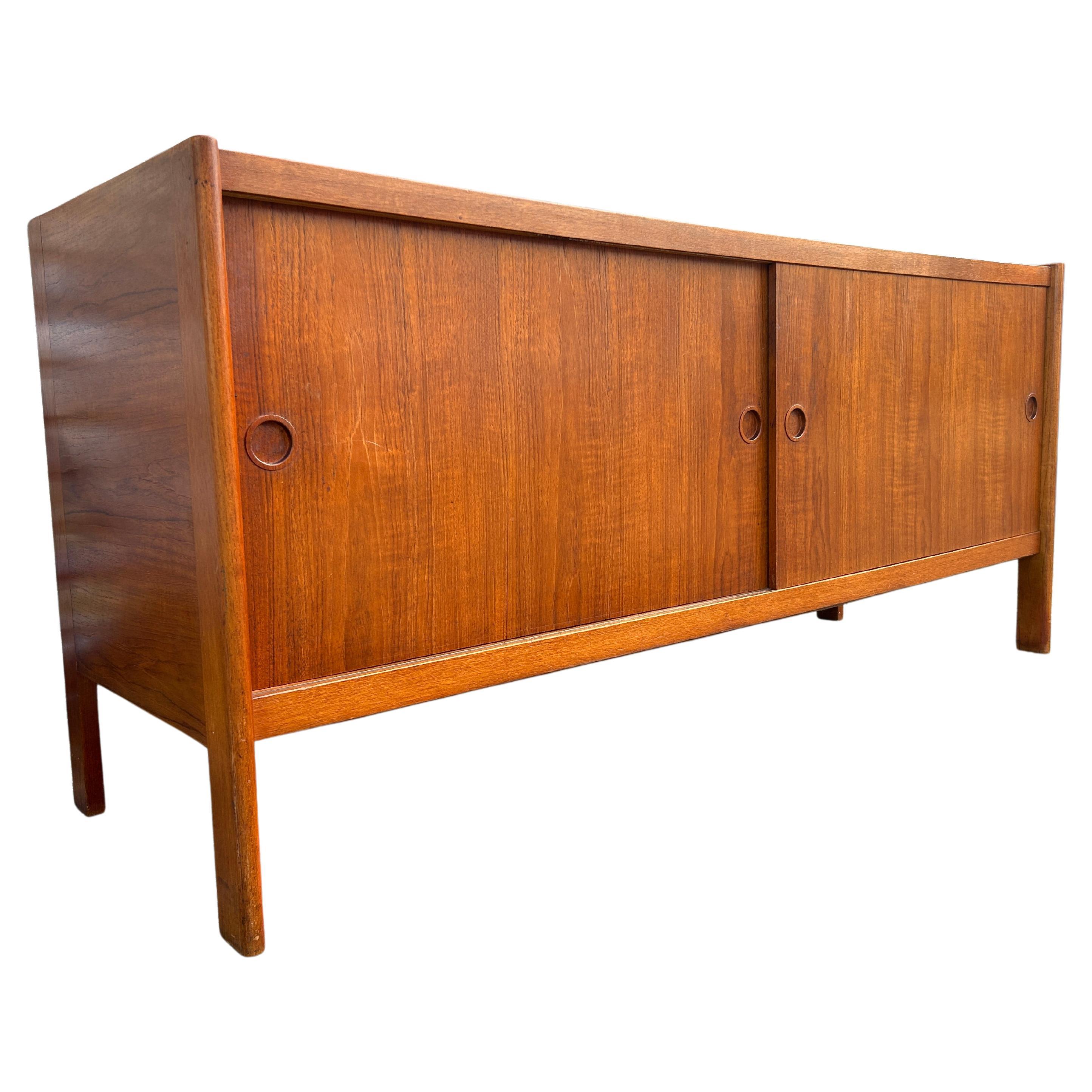 Midcentury Danish modern teak sliding door credenza by Poul Hundevad. Has 2 front sliding doors with round carved teak handles. Has 2 adjustable shelves w/pins in each section also has 1 narrow teak drawer on the right top of inside the credenza.