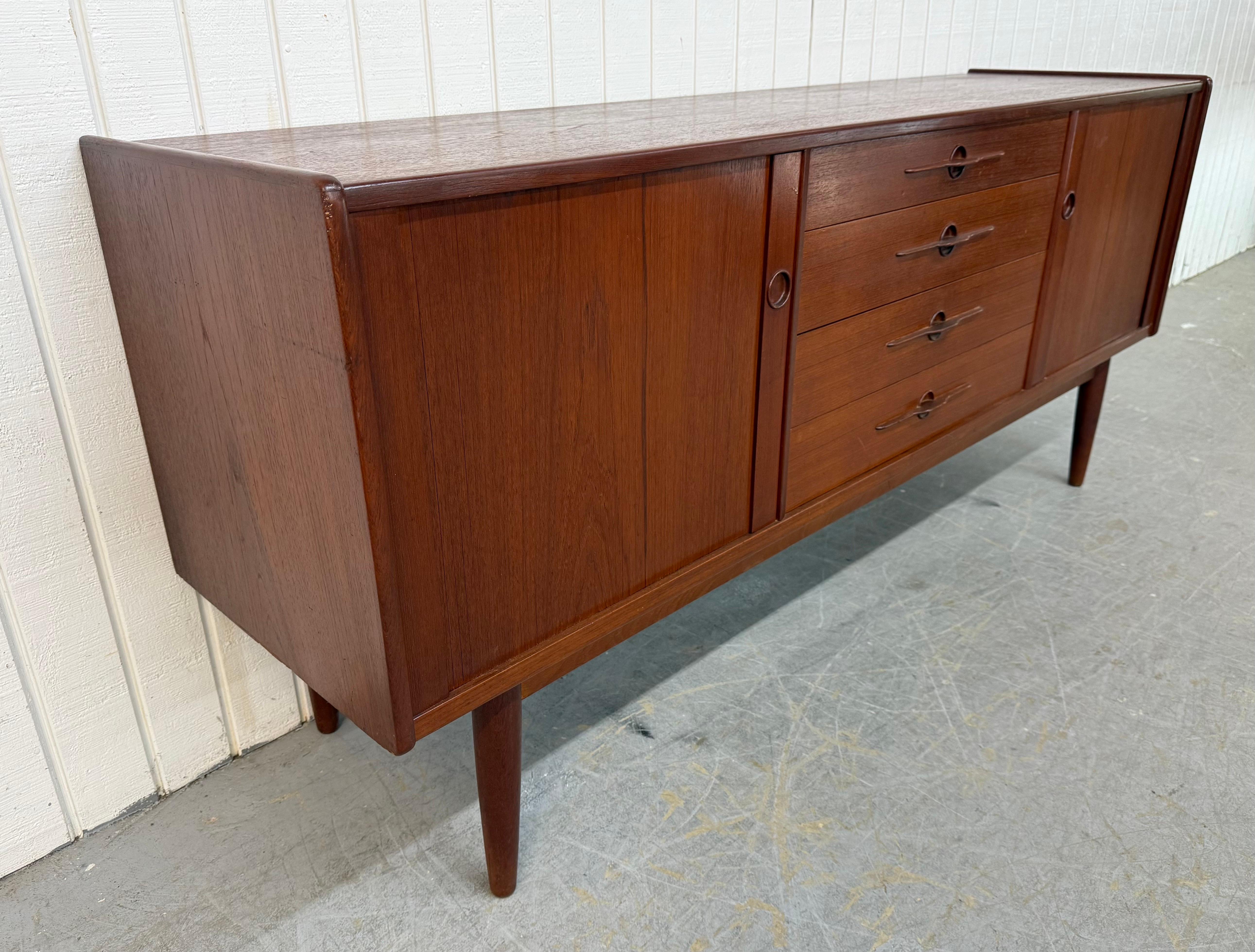 This listing is for a Mid-Century Danish Modern Teak Tambour Sideboard. Featuring a straight line design, rolling tambour doors on each end that open up to storage space, four center drawers with sculpted wood pulls, modern legs with a stretcher