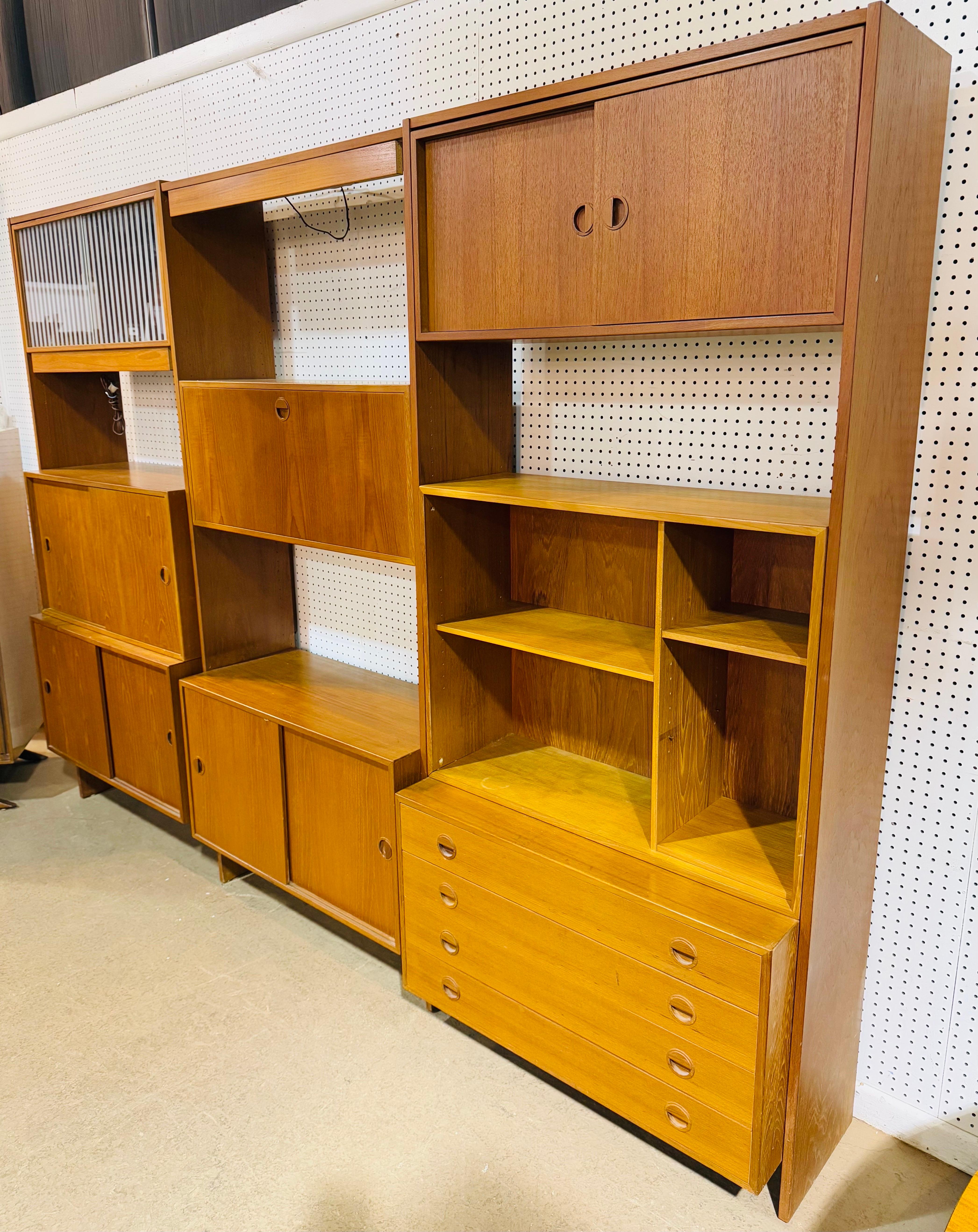 Questo annuncio si riferisce a un mobile da parete in teak di stile danese moderno di metà secolo. Caratterizzato da un design lineare, tre sezioni di armadietti, porte scorrevoli multiple che si aprono per creare spazio di archiviazione, armadio