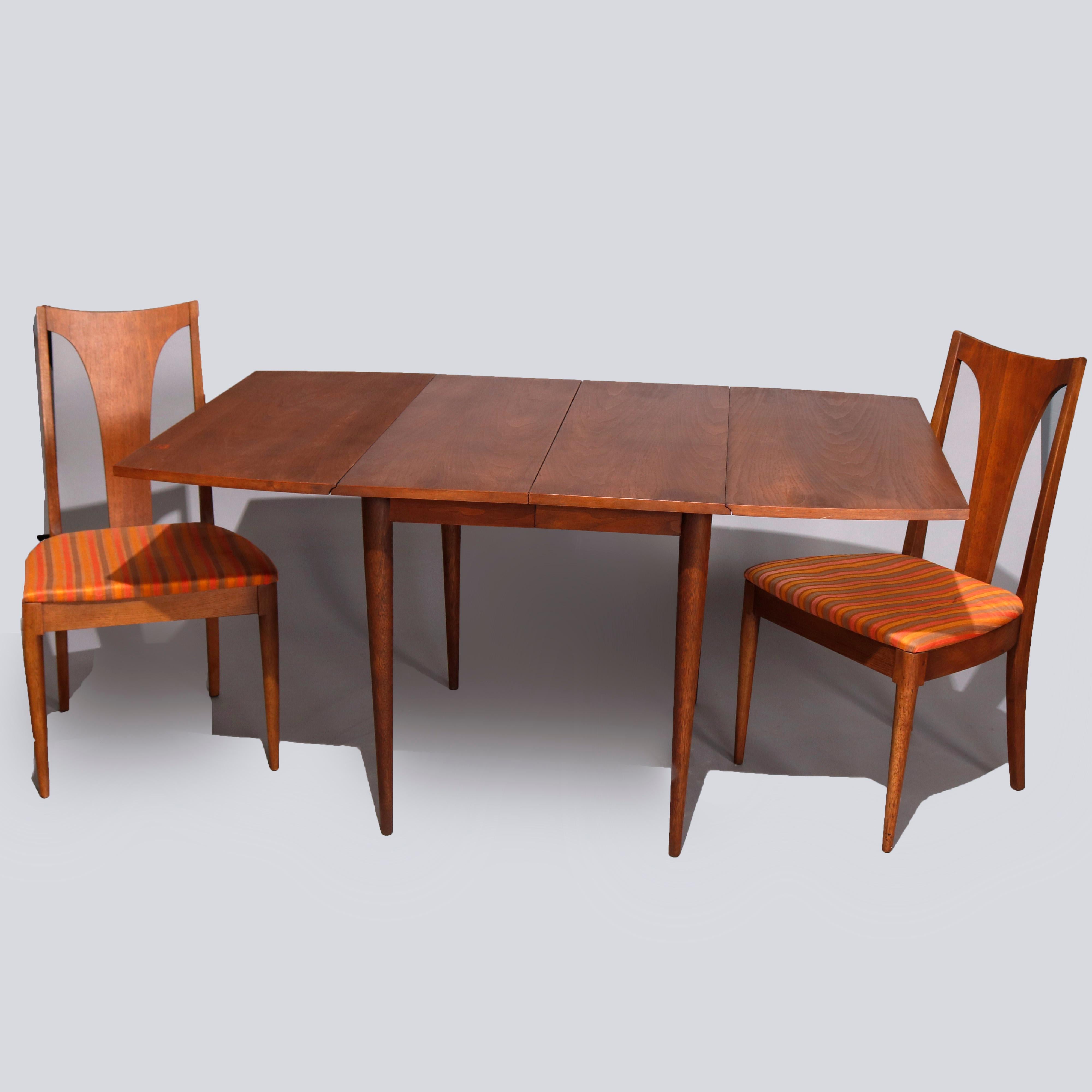 A midcentury Danish modern dining set by Broyhill offers walnut construction and includes extension dining table with three leaves raised on turned and tapered legs and four chairs with stylized curved T-backs and upholstered seats, 20th