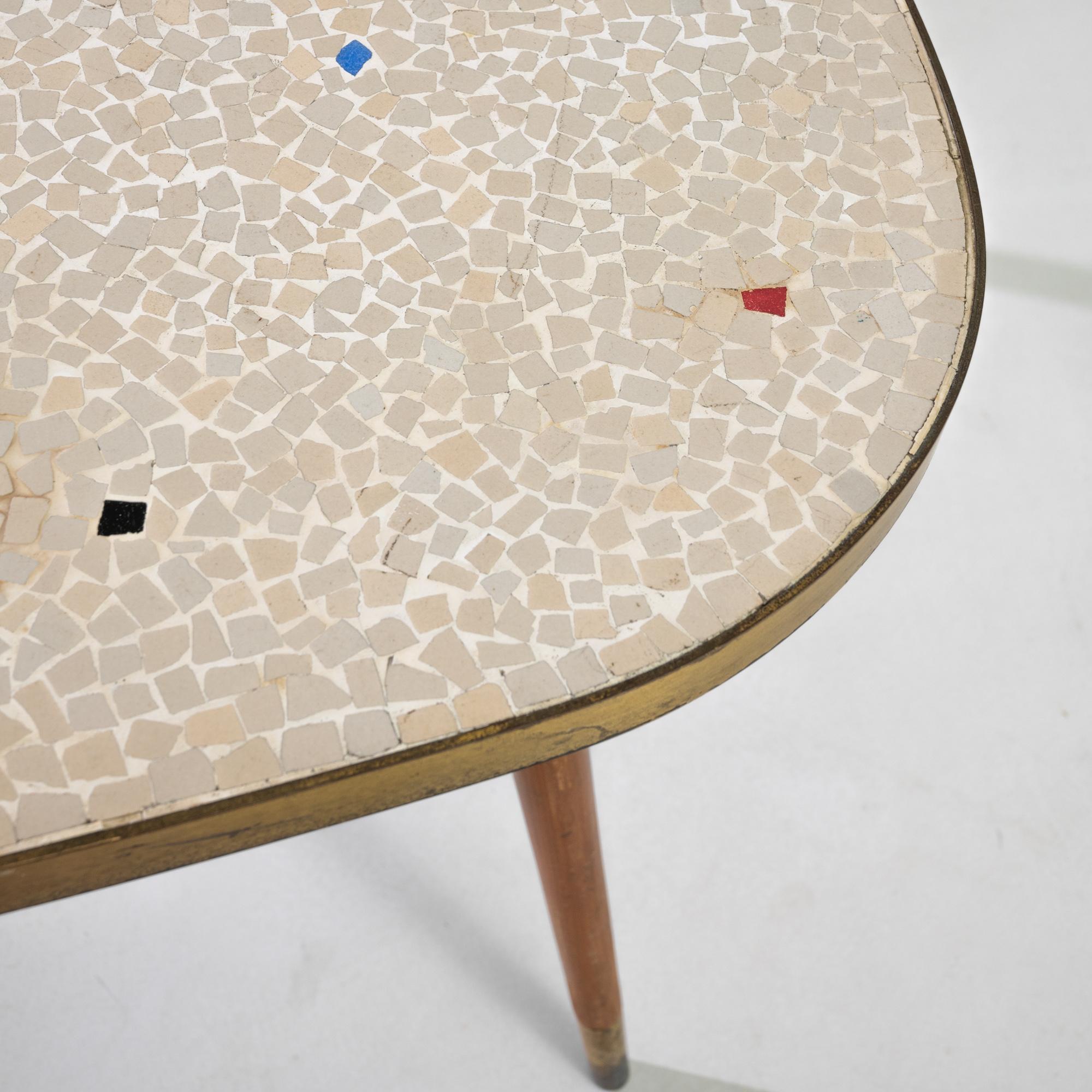 Joyful and idiosyncratic, this wooden coffee table illustrates the playful side of Scandinavian Modernism. Made in Denmark in the 1960s, an ovoid mosaic tabletop sits atop a trio of tapered wooden legs. The cream tiles of the mosaic are punctuated