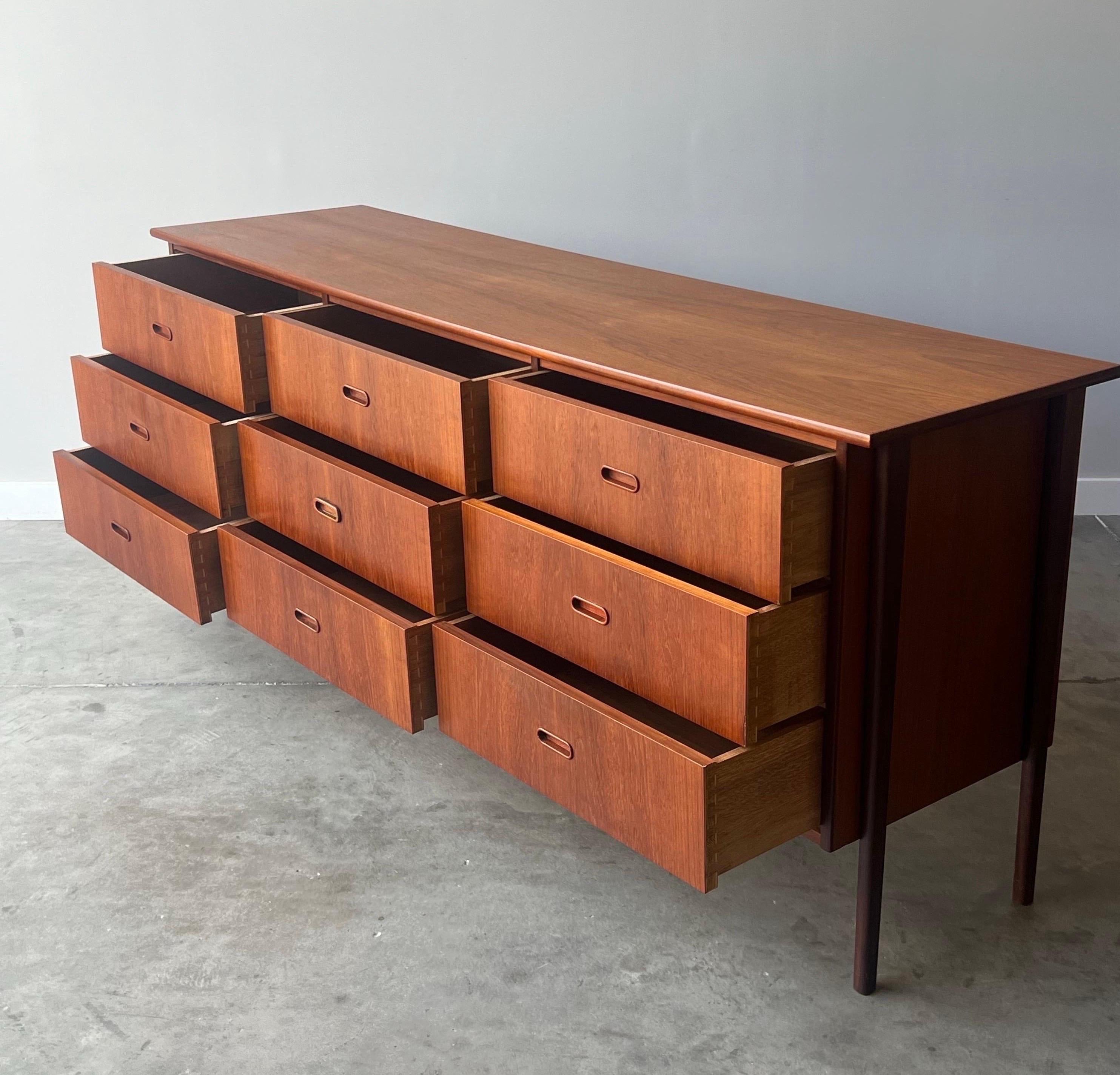 Mid-century Danish teak dresser featuring nine drawers. This piece would be an excellent addition to any style bedroom. The drawers are spacious with carved inland oval fronts. The top of the credenza extends beyond the body which is both eye