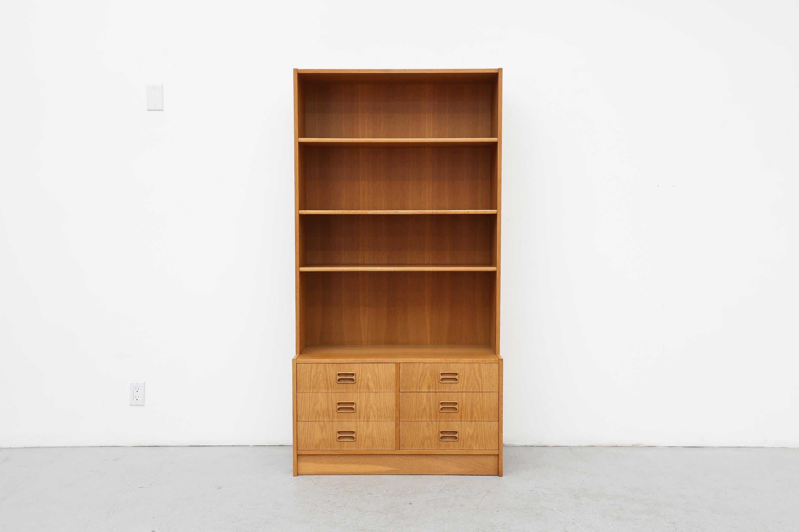 Niels Andersen designed,  oak, standing 2 piece bookcase. Lower cabinet has four drawers, the upper portion has shelves. Two are available, one has a small cutout at the bottom middle of the shelving portion for a cord to go through. Both in