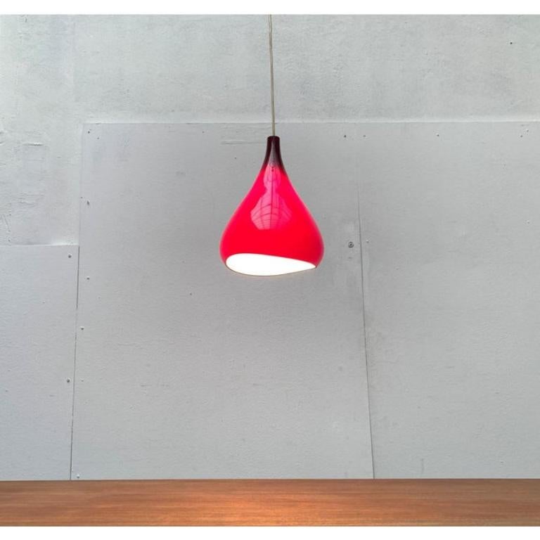 Lampada a sospensione in vetro Krokus del produttore danese Nordisk Solar su progetto di Sigvard Bernadotte e Acton Bjørn degli anni '60.

Il corpo dell'apparecchio, a forma di goccia, è realizzato interamente in vetro opalino e rosso scuro