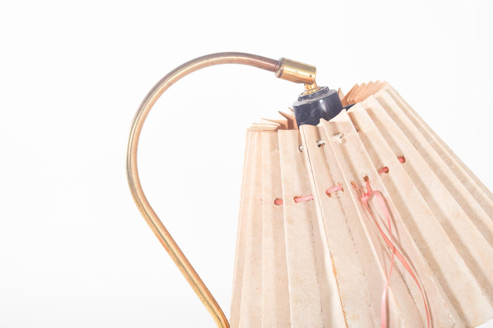 Pair of metal table lamps. With an arched metal structure and a gold finish, they stand on flat circular bases. Each one is topped by a beige abat-jour made of paper folded into a pelmet, with hand-stitching in pink thread, a detail that adds a