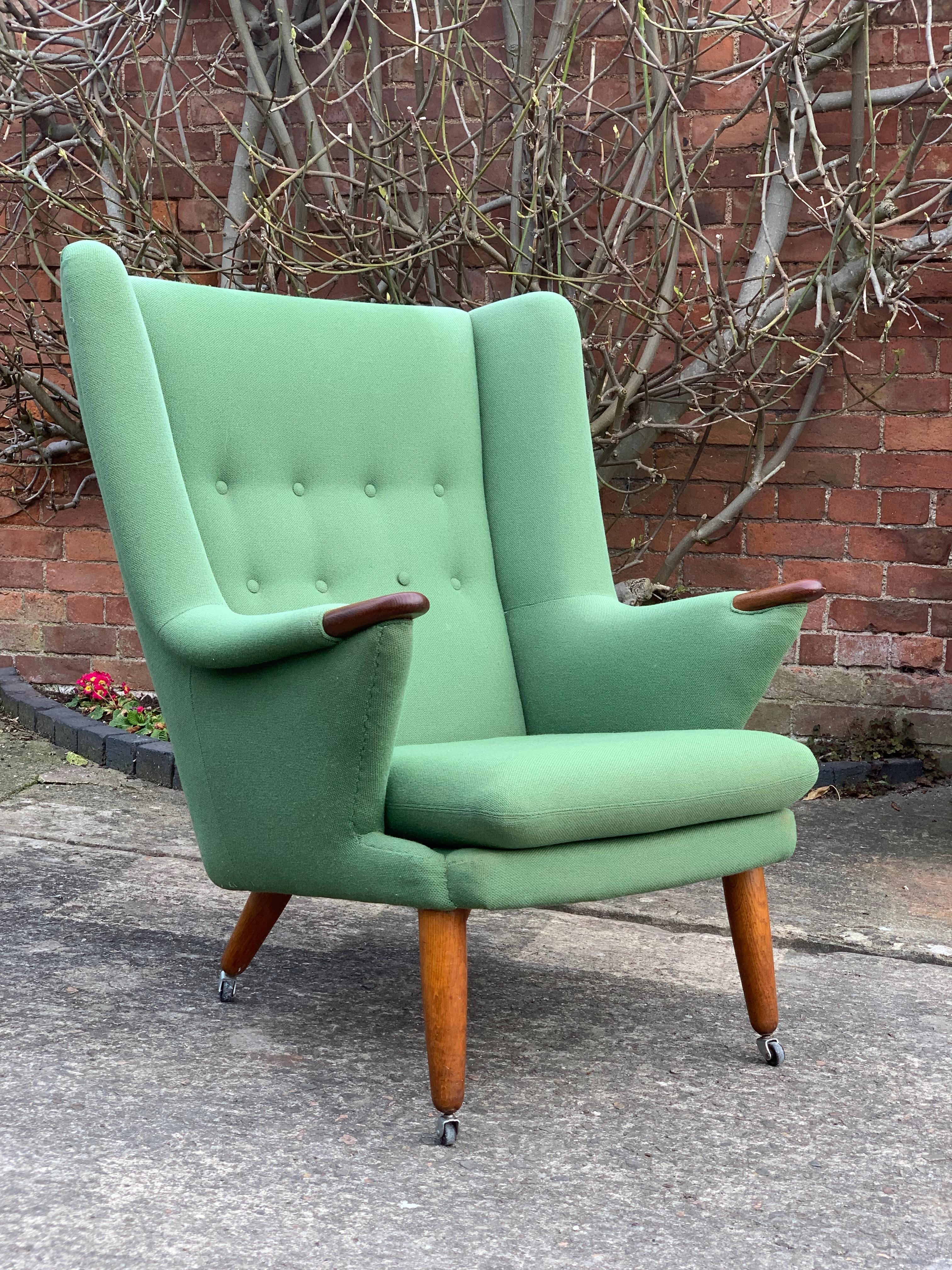 Midcentury Danish ‘Papa Bear’ armchair, circa 1950s, the pea-green fabric upholstered wing armchair, in the manner of Hans Wegner, having a buttoned back, with oak finished arm rests paws, on conforming turned and tapering supports to castors.

 