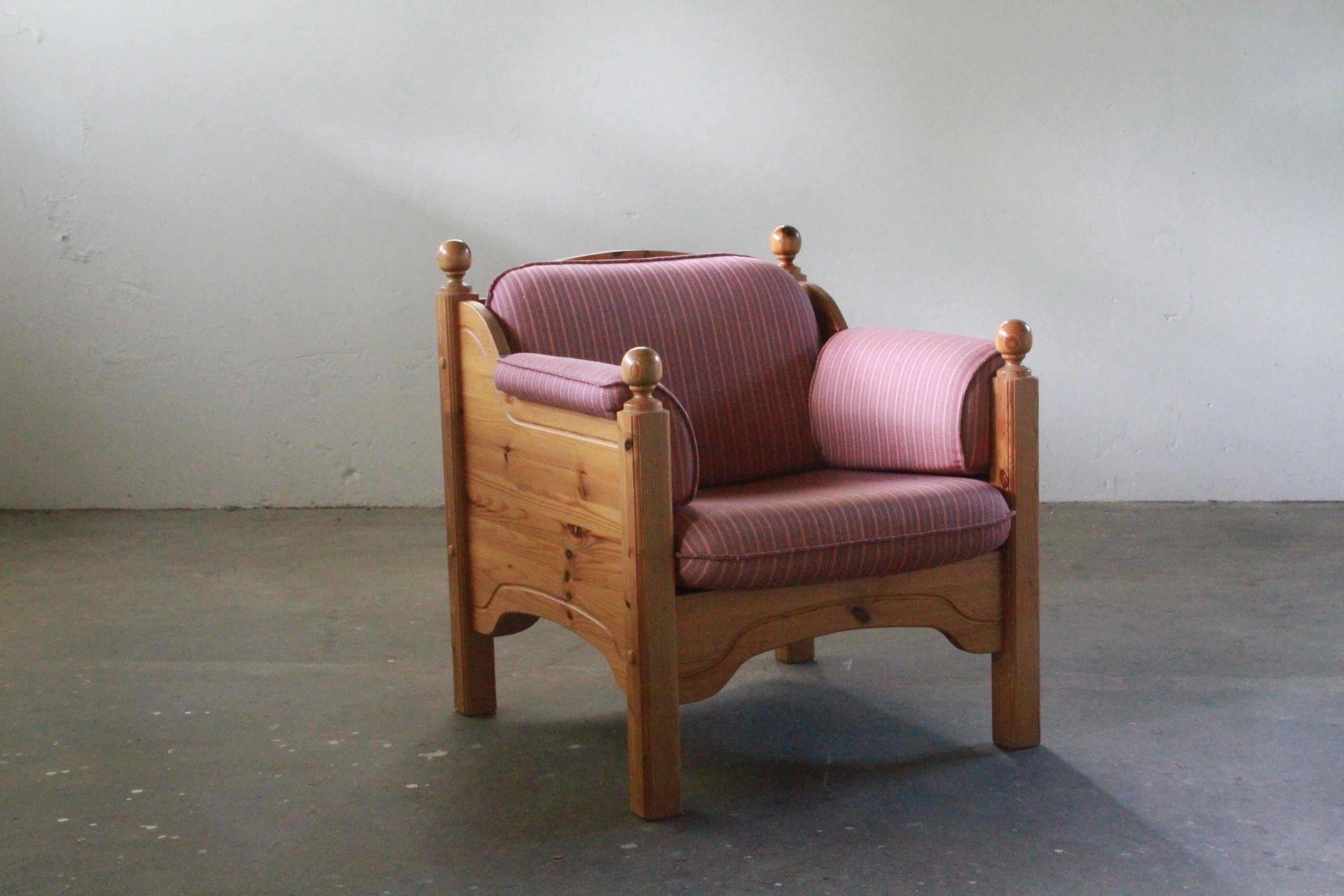 Danish pine lounge chair, gracefully aged with a natural patina. The robust wood features a well-maintained varnish, ensuring enduring stability. Its weight anchors a subtle sense of coziness, offering a timeless charm to any space. The cushions and