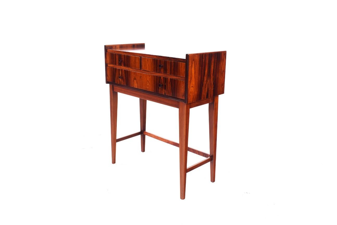 Single elegant midcentury nightstand/bedside table in rosewood and rosewood veneer, with dynamic pattern matched grain. The table consist of two drawers on top with one big drawer below and elevated legs.