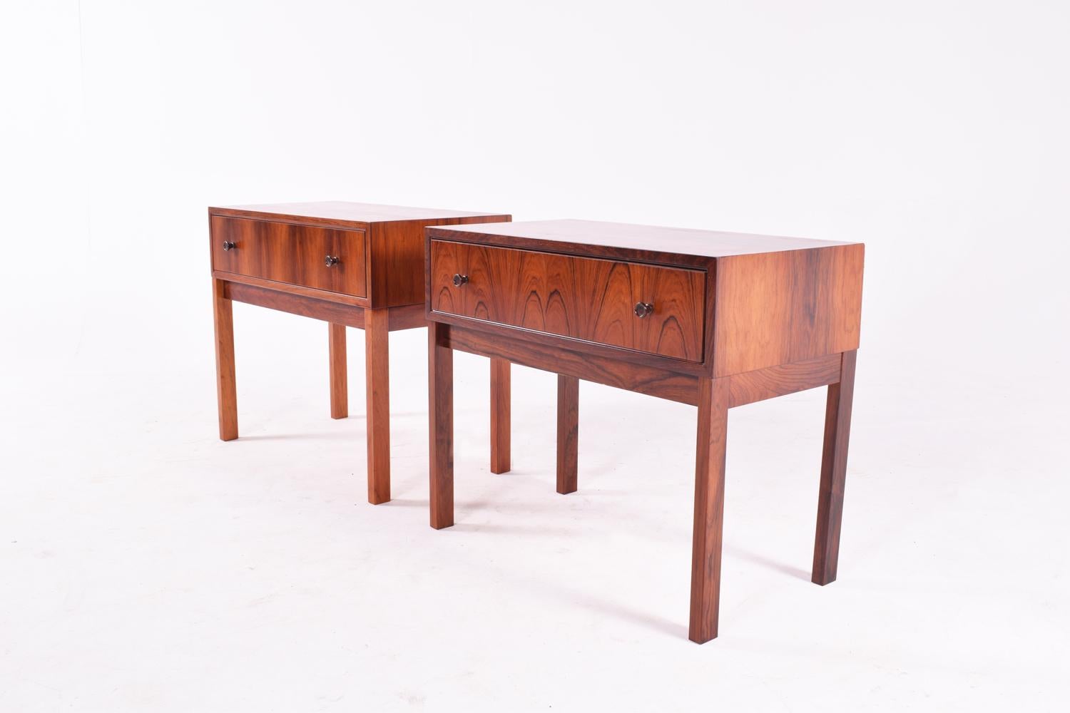 Pair of Danish modern bedside tables in rosewood from the 1960s. Each bedside table has a front drawer and two pull buttons. Slightly different veneer, same model. Elegant and vivid rosewood veneer.