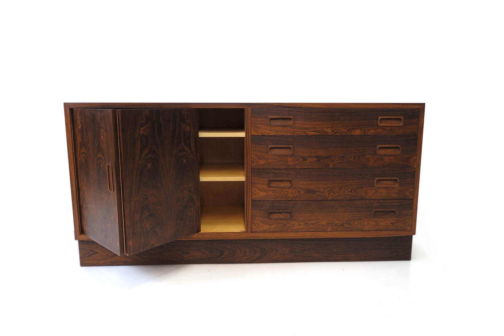 Danish rosewood cabinet handcrafted of stunning Brazilian rosewood with book-matched grains across the front, mitered corners on the cabinet, two bi-fold doors with adjustable shelves, and series of four drawers. The cabinet is raised on a plinth