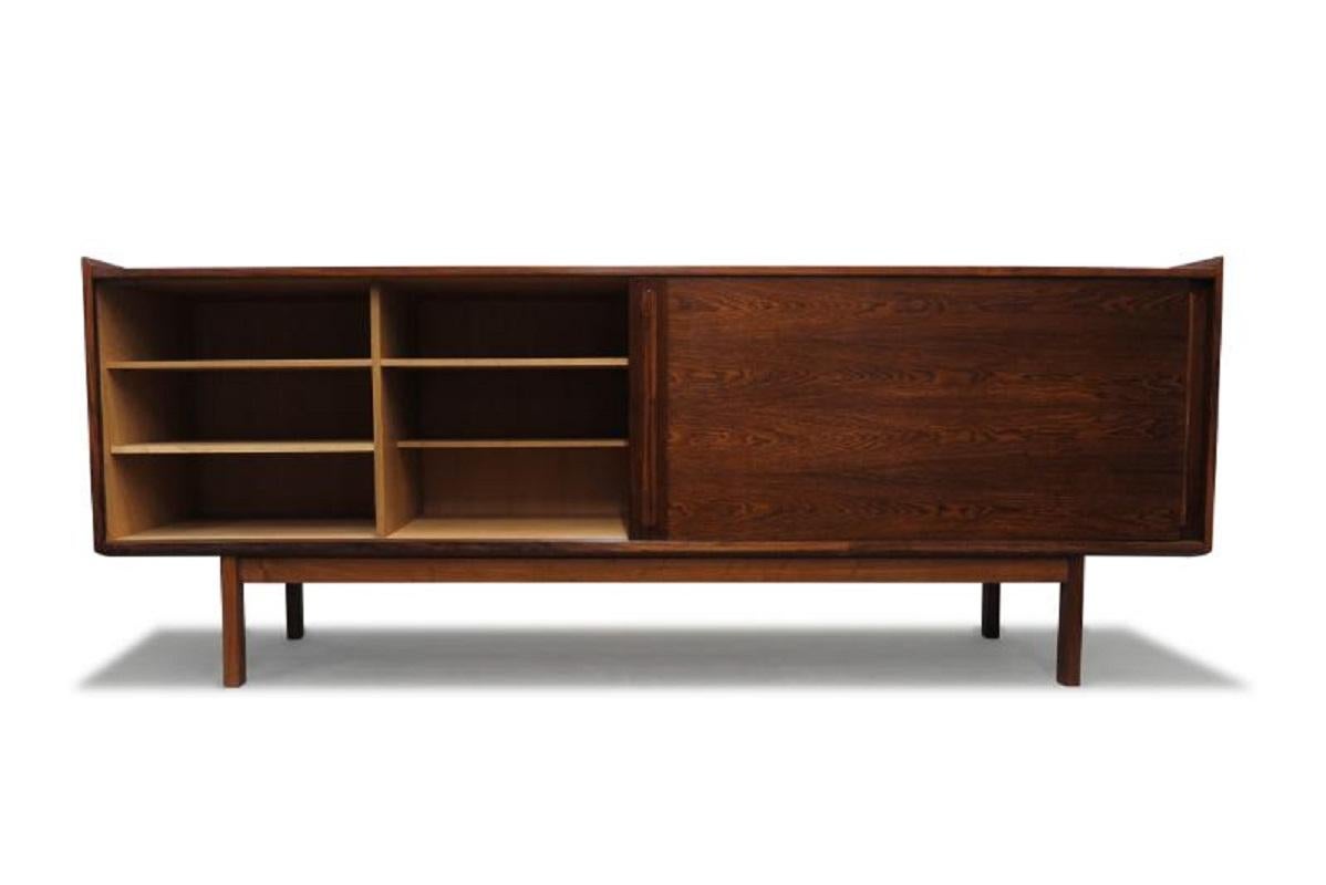 Early 1950s Danish credenza finely handcrafted of Brazilian rosewood, featuring a pair of sliding doors with book-matched grain, opening to reveal an interior of white oak with adjustable shelves and silverware drawers. Raised on squared rosewood