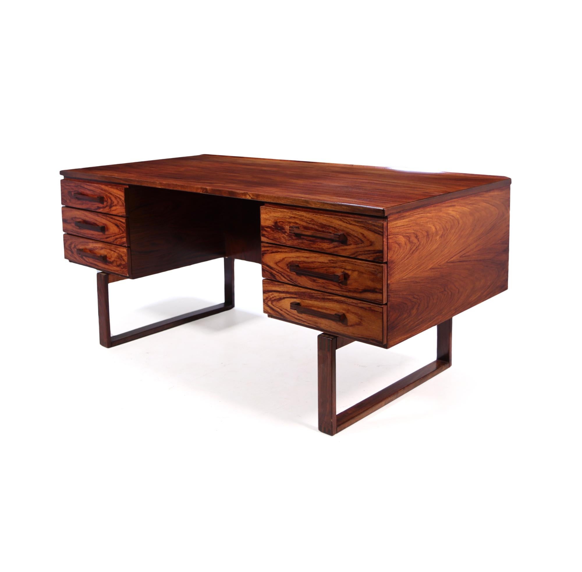 Designed by Henning Jensen and Torbin Valeur in Denmark in the mid 1960's. This rosewood desk has beautiful graining to the desk and has exposed finger joint construction sled feet and on the drawer handles. Highlighted by a subtle raised lip along