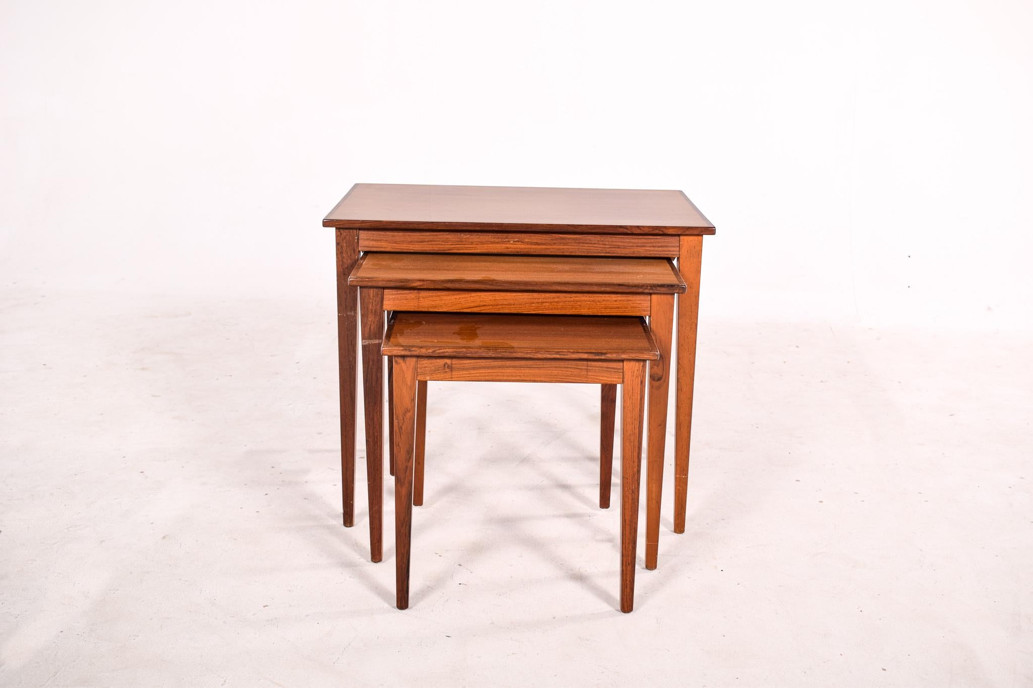 Set of three Danish nesting tables, made of rosewood. Table design has square, slightly recessed legs, and a tabletop beautifully edged with contrasting wood grain. A set of concealed, parallel runners allows each smaller table to slide easily under