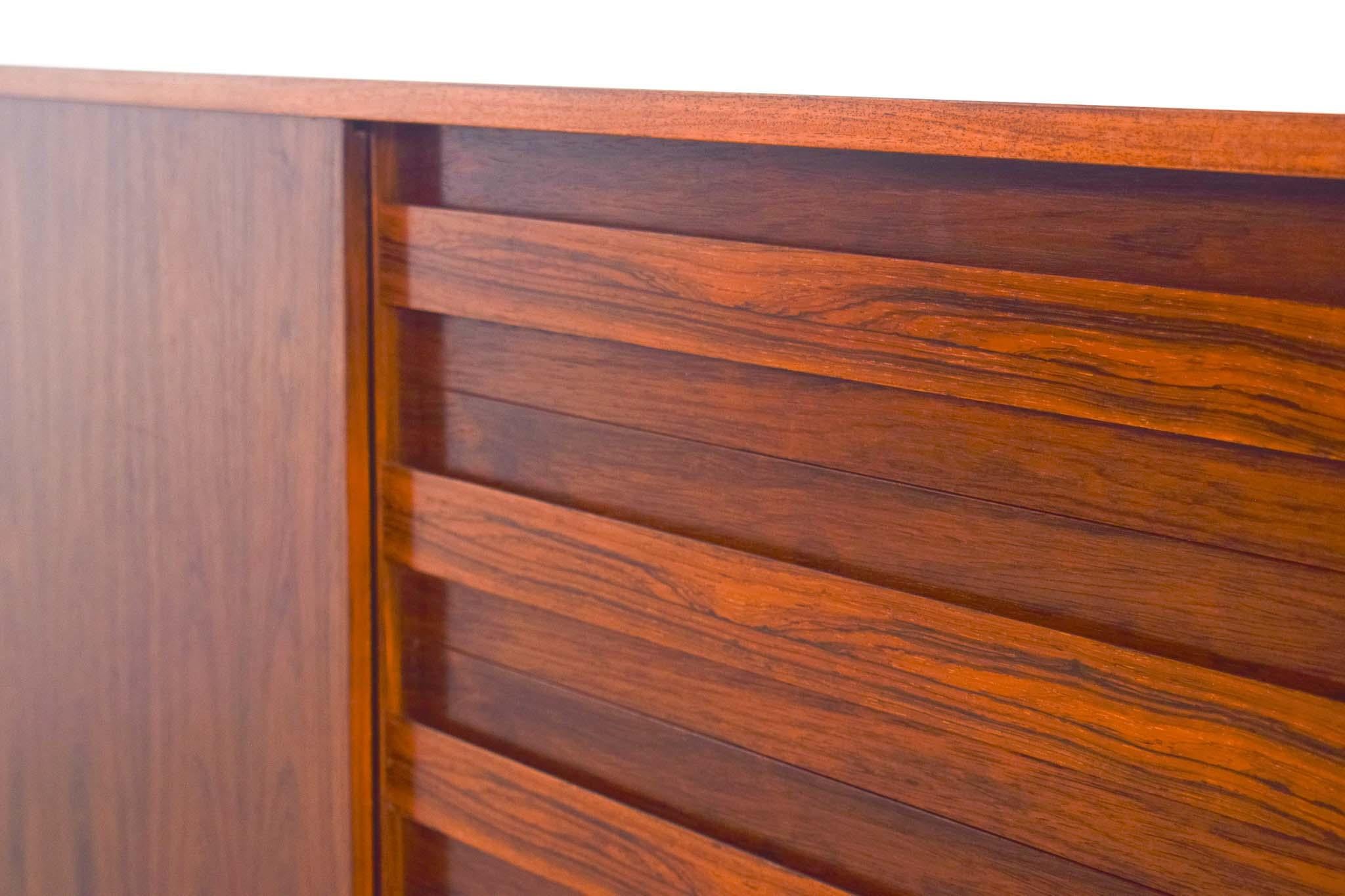 Ce buffet danois des années 1950, fabriqué dans un luxueux bois de rose, respire l'élégance du milieu du siècle. Il présente un agencement bien pensé avec quatre tiroirs, une porte coulissante et une étagère, offrant des options de rangement