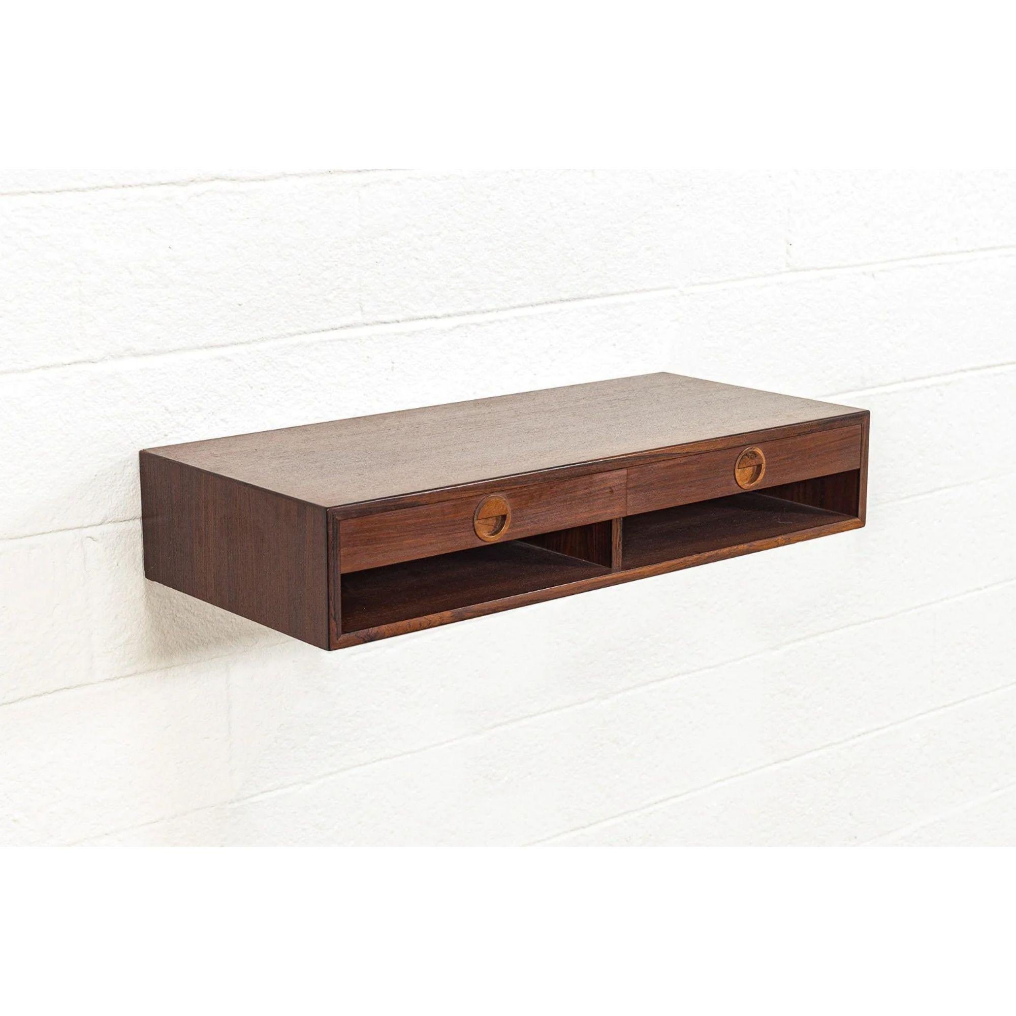 This vintage Mid-Century Modern Hansen & Guldborg wall-mounted floating shelf made in Denmark circa 1965 has a Classic Scandinavian Modern design with clean, Minimalist lines. Well-built from rosewood, the cabinet features a lower cubby shelf and