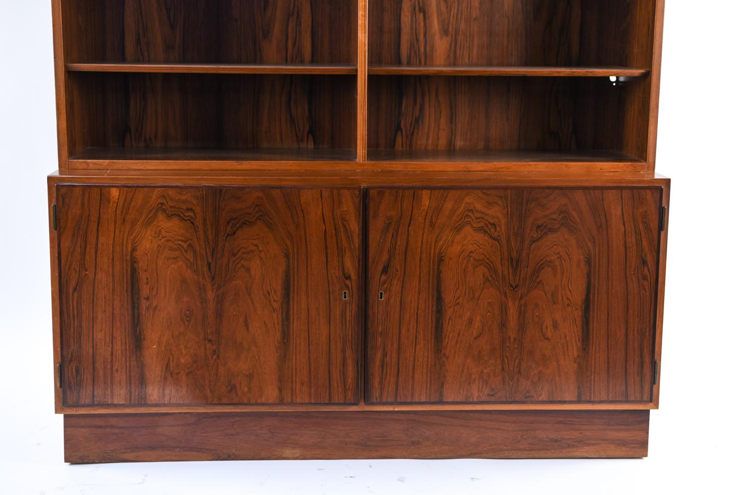 A Danish midcentury wall unit by Omann Jr. A double bookcase sits upon a cabinet beneath providing ample storage, both for display and hidden. This beautiful piece with bookmatched rosewood will be the highlight of any wall.