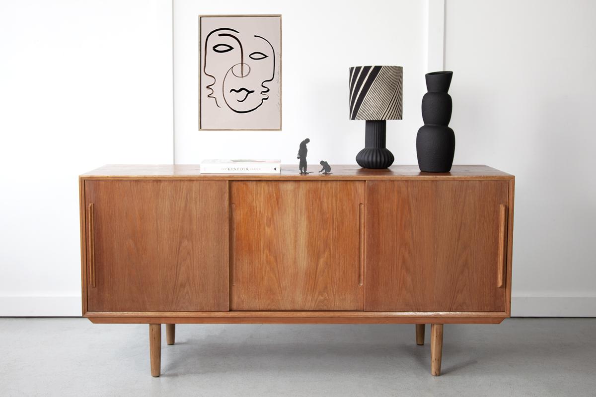 A quintessential Danish sideboard in oak, combining sleek design with a practical storage solution. The sliding doors house shelved storage compartments and two small drawers. Displaying lovely grain detailing and a warm rich tone, this sideboard is