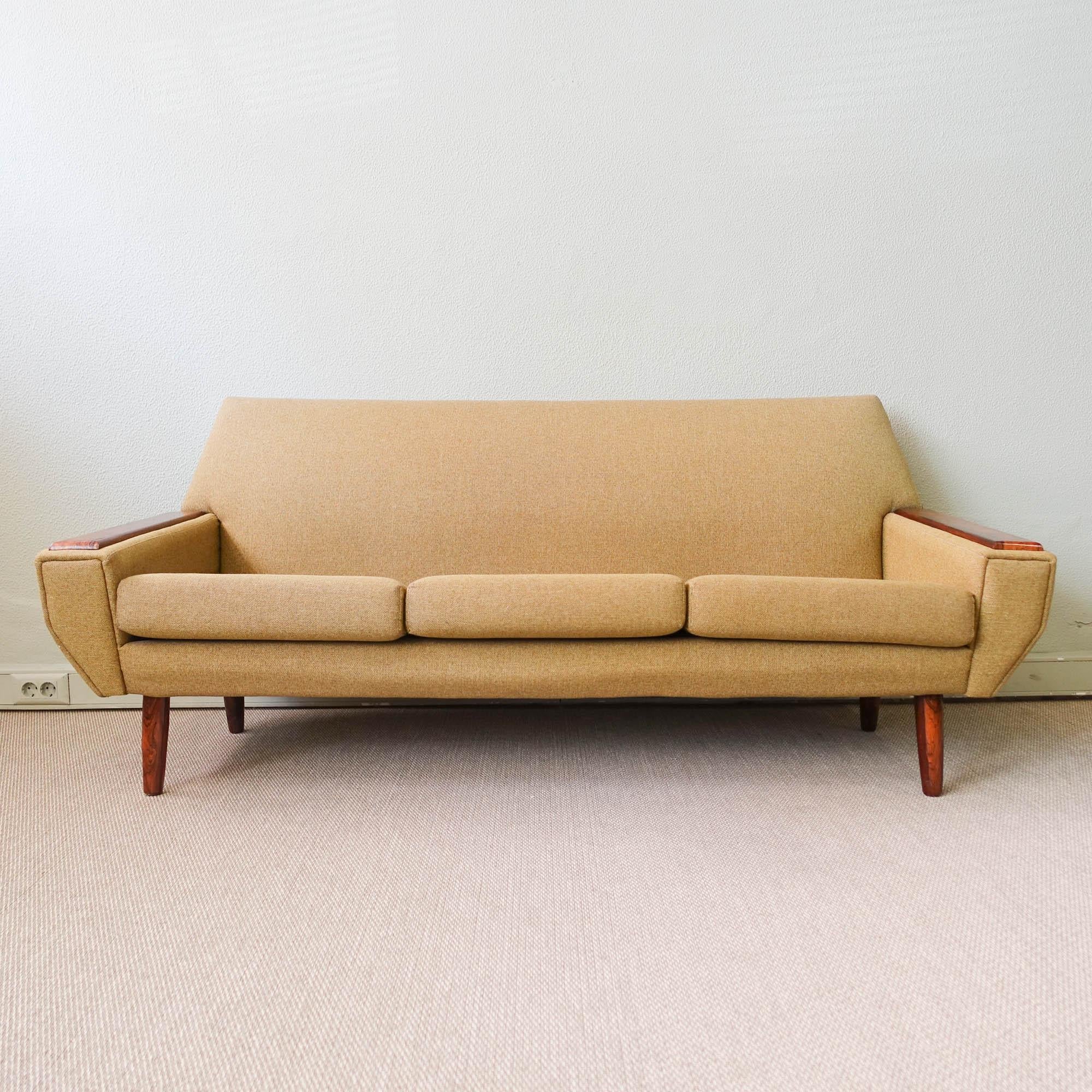 This sofa was designed and produced in Denmark during the 1960's. It is a three seater sofa has with an unique contoured shape, and features exotic wood armrests and feet. The green fabric is in good vintage condition, with some marks related with