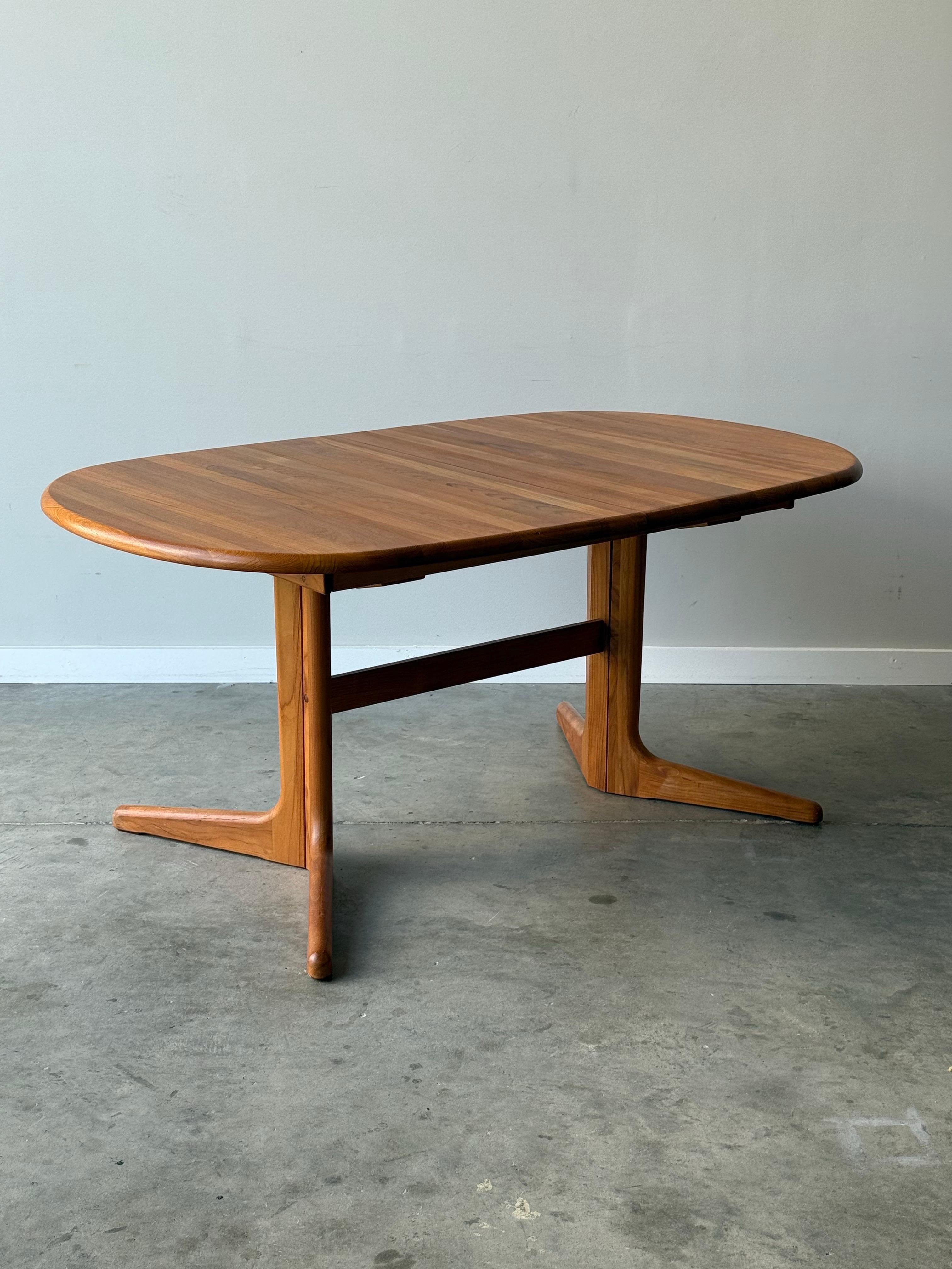 Mid-century dining table made from solid teak wood. Manufactured in Denmark, circa 1970s. Oval shaped top with one removable leaf. Leaf can be stored within the table for easy accessibility and storage saving. The tabletop is on a smooth sliding