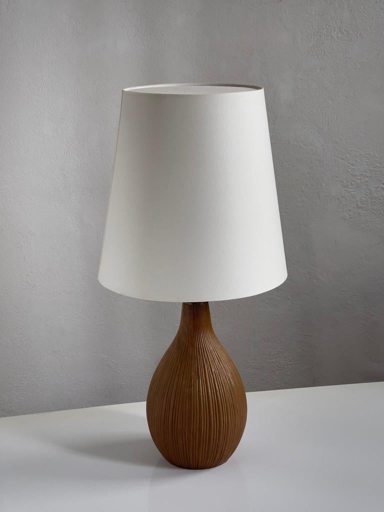 Cette lampe de table unique en grès danois du milieu du siècle est une superbe représentation des principes du design scandinave, intégrant harmonieusement la forme, la fonction et les matériaux naturels. Le corps de la lampe, rendu dans une teinte