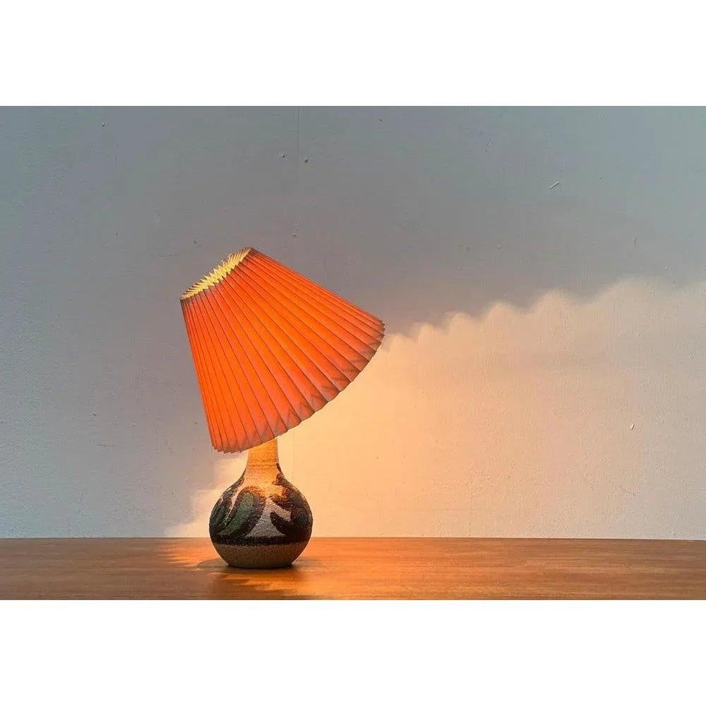 Ceramic table lamp from the Danish manufacturer Søholm from the 1960s.

The conical pleated umbrella sits directly on the lamp with a bracket. This type of recording enables manual alignment of the umbrella. The ceramic foot shows a colored decor