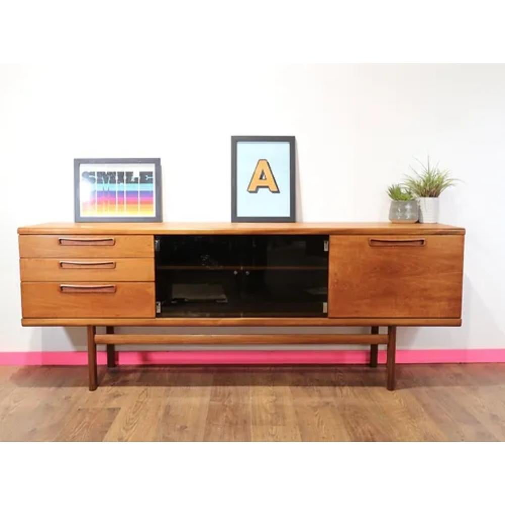 Introducing the stunning Mid Century Danish Style Teak British Credenza Sideboard by Meredew. This beautiful credenza by English furniture maker Meredew is a rare beast, with a great color and grain, and the black glass doors really make this stand