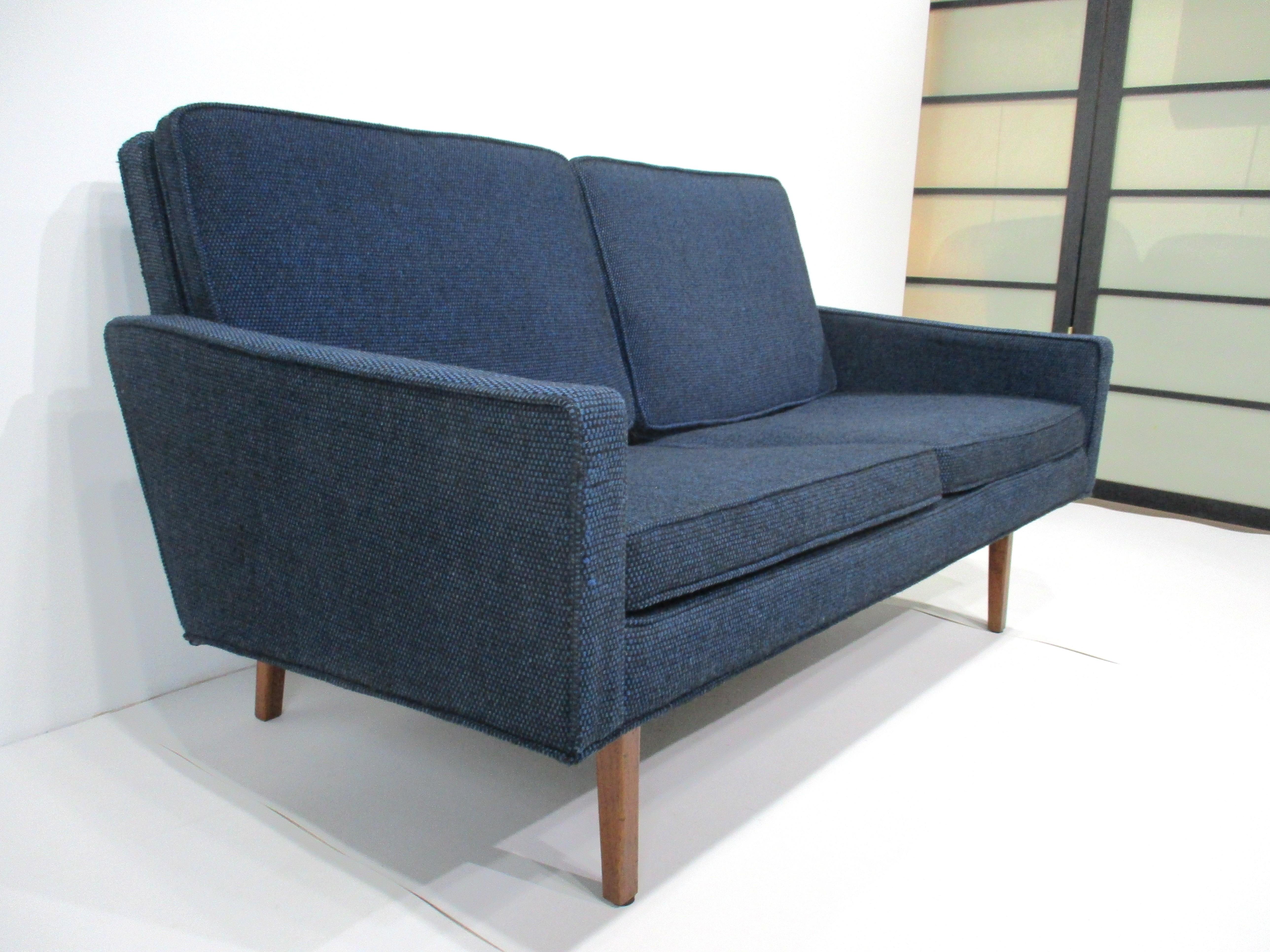 A very nice sized Danish styled Mid Century loveseat upholstered in a tight woven blue contract fabric which is original to this piece . Framed in a medium dark walnut with great back stretcher and matching legs makes this functional piece perfect