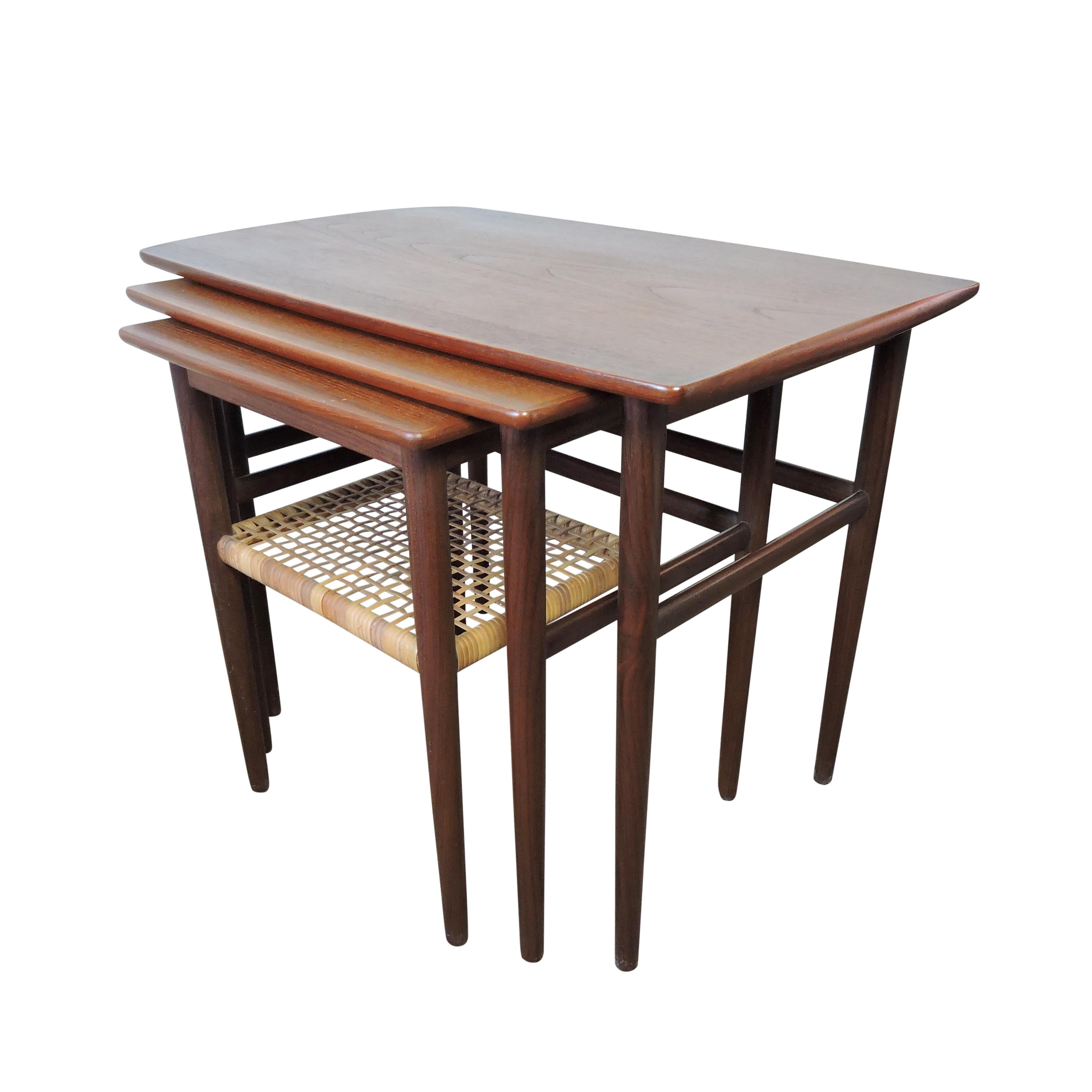 A 1950s midcentury set of nesting tables, designed and manufactured in Denmark. They are made of teak with a shelf made of cane.