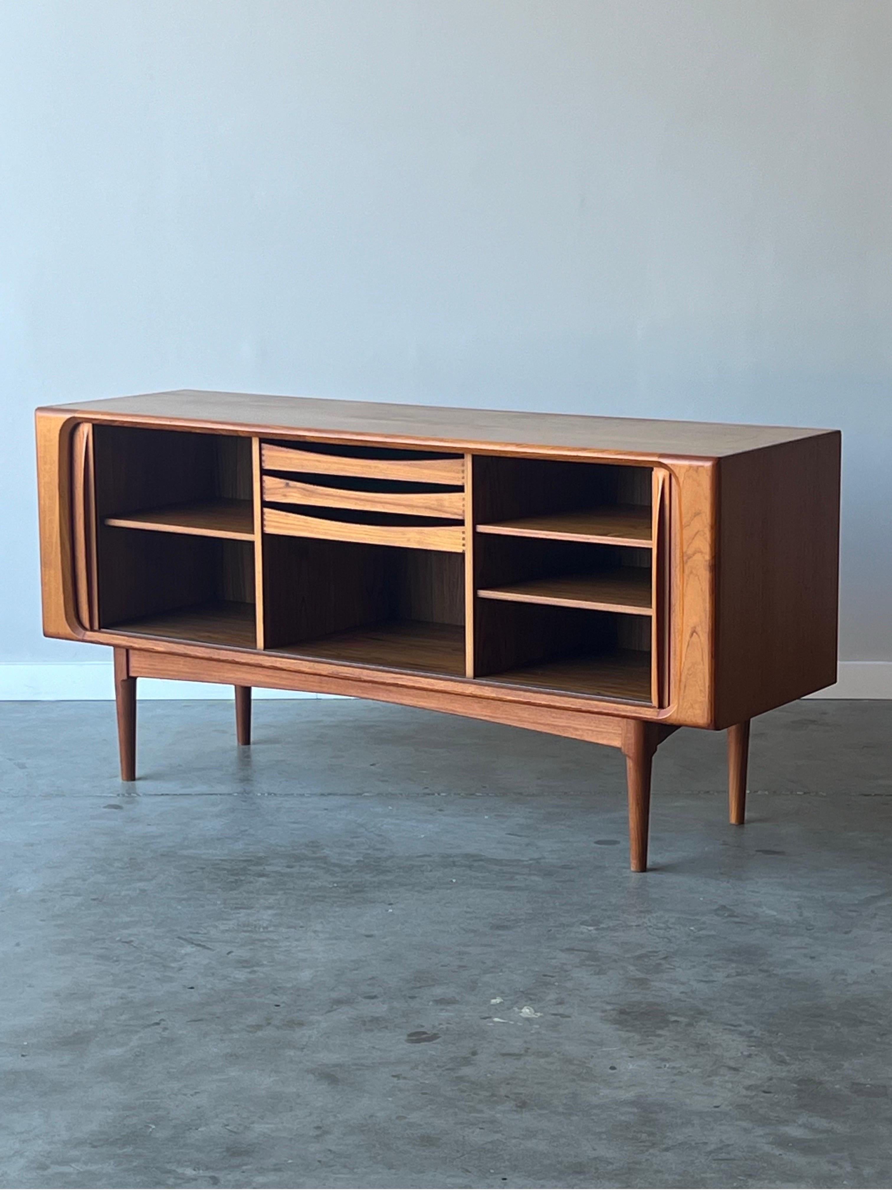 Mid-century credenza designed by Bernhard Pedersen and Son, Denmark. This 1970s credenza is made from teak and features two tambour doors and beautifully sculpted handles. The doors slide smoothly and with ease. Inside the credenza, there are three