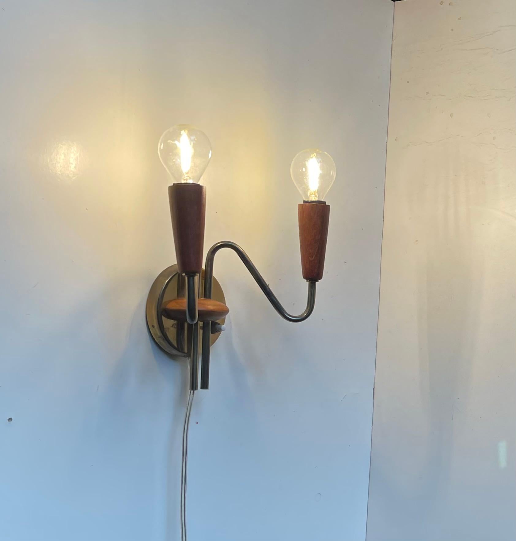 Aplique doble (dos fuentes de luz) de teca y latón con diseño tubular, fabricado en Dinamarca en la década de 1950 en un estilo que recuerda a Stilnovo.   

Medidas: Alto: 25 cm, Ancho: 20 cm, Fondo: 13 cm.

Para los EE.UU. Vendrá instalada con un