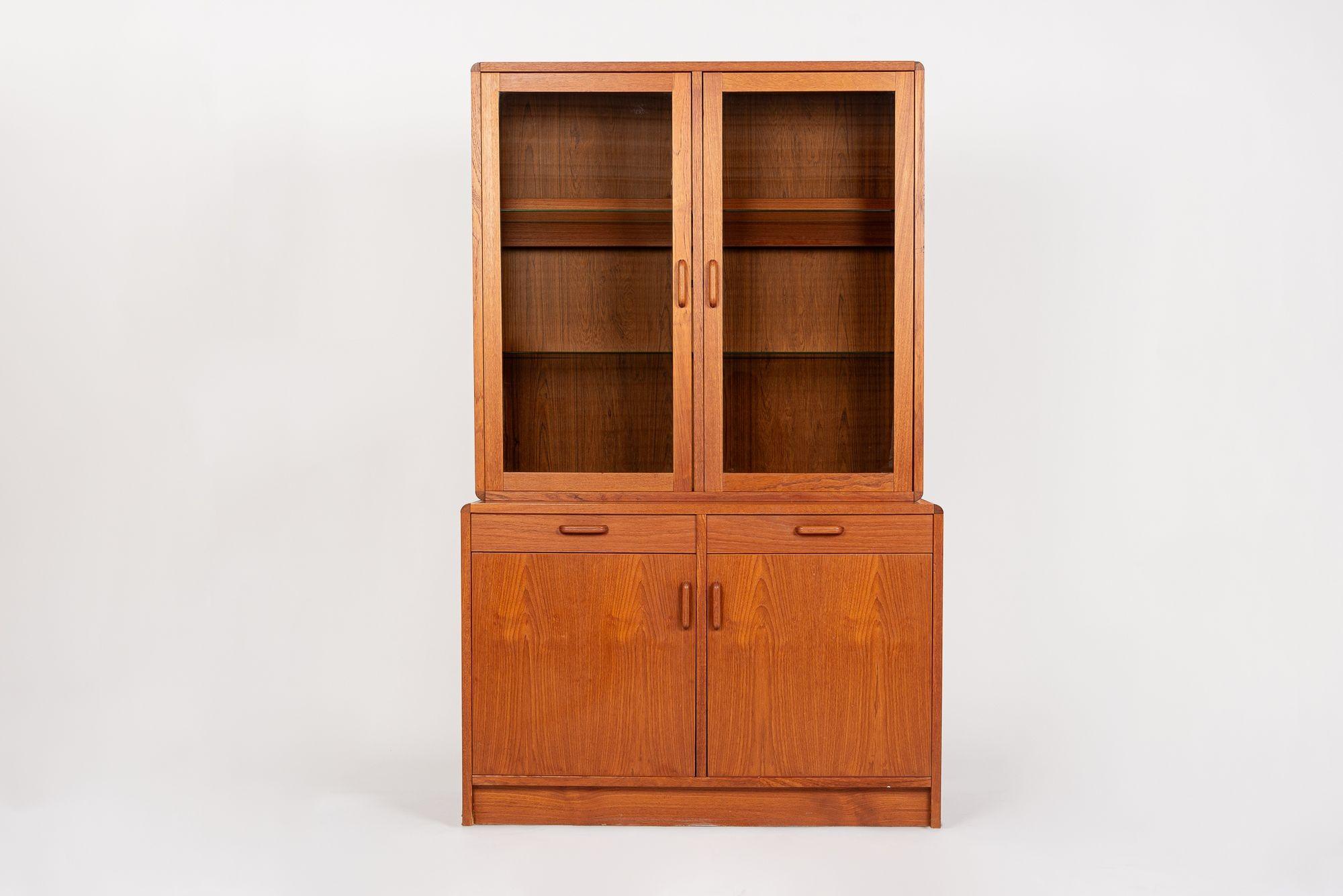 This vintage mid century modern step-back teak lighted china cabinet or display case wall unit was made in Denmark by STM Mobler circa 1970. This lovely cabinet is elegantly proportioned with clean, minimalist lines and is well-crafted from teak