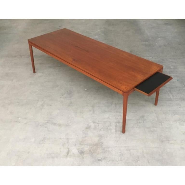 Langer Couchtisch des dänischen Herstellers Anton Kildeberg.

Der Tisch ist ein zurückhaltenderer Gebrauch der Form. Die Tischplatte ist rechteckig und nur leicht gerundet. Und die Grundplatte ist optisch durch einen Schatten getrennt. Die Beine