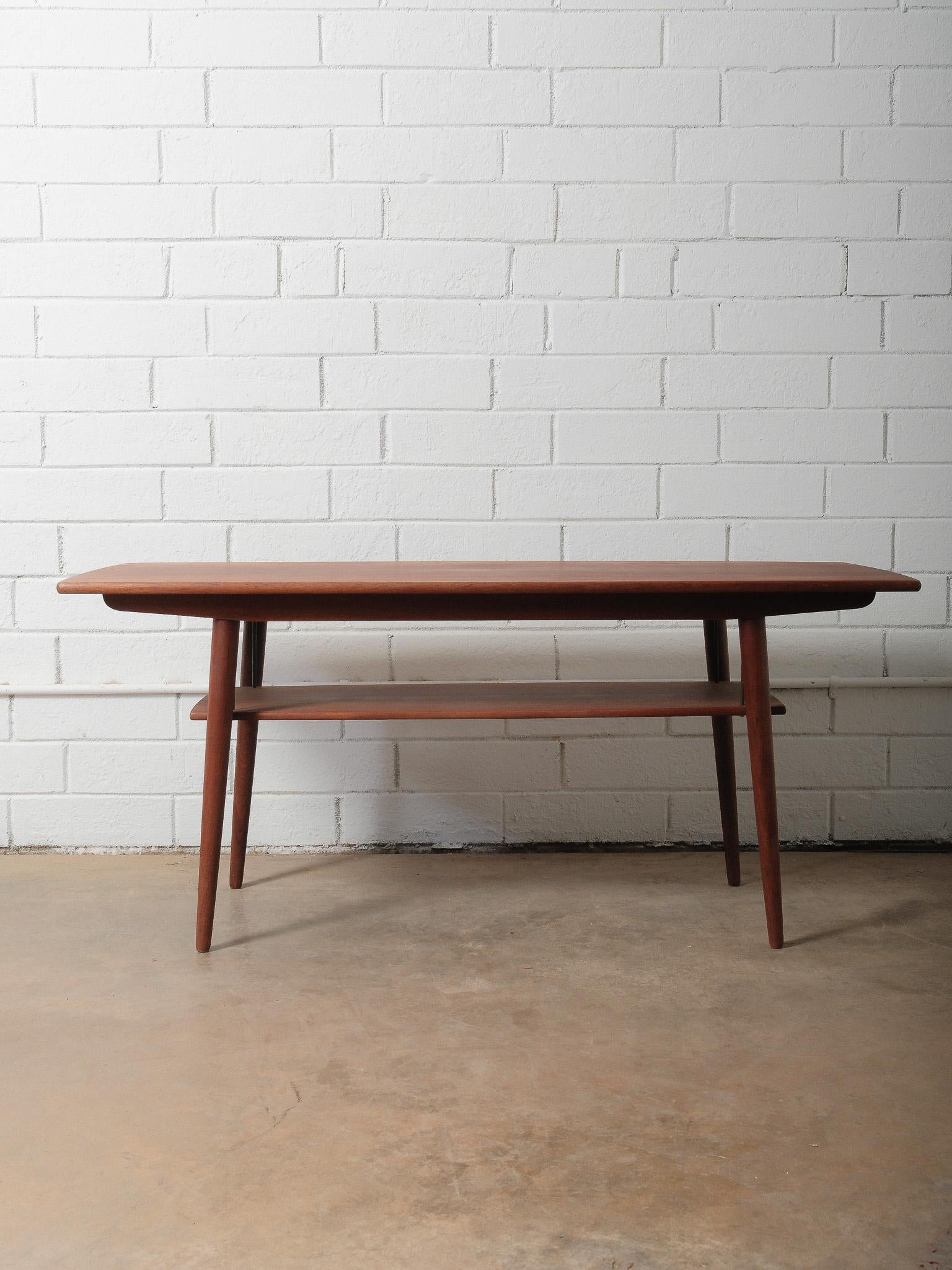 A beautifully crafted Mid-Century Danish teak coffee table featuring clean lines, soft rounded edges, and a warm, even-toned finish. Its signature floating lower shelf adds both visual lightness and practical function, perfect for storing books,