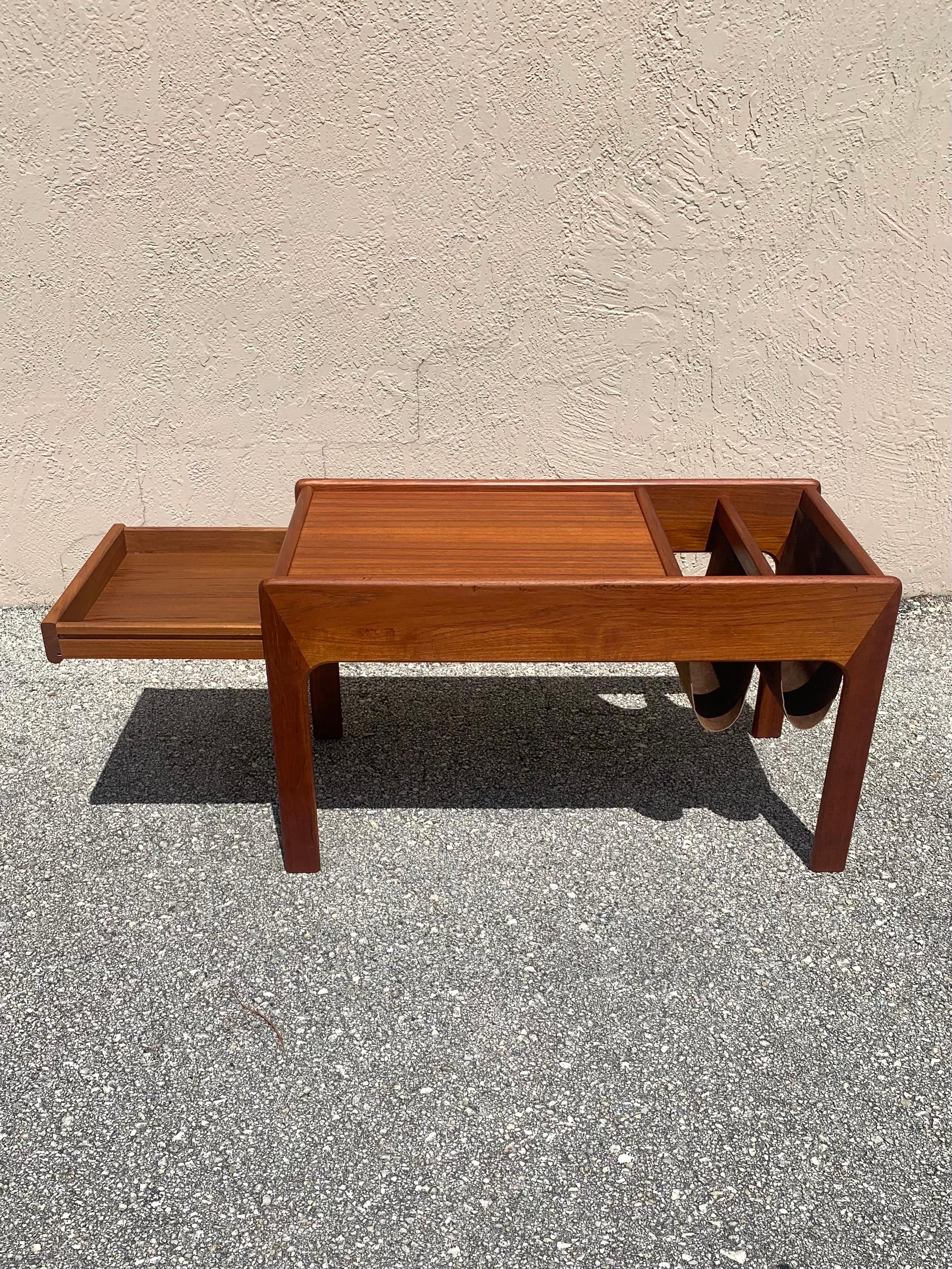 Mid-Century Modern coffee table and magazine rack. Made in Denmark. Stunning natural grains pair beautifully with the suede magazine slings. 

The frame of the table is made from solid teak wood. The table top is teak veneer. On the side there is