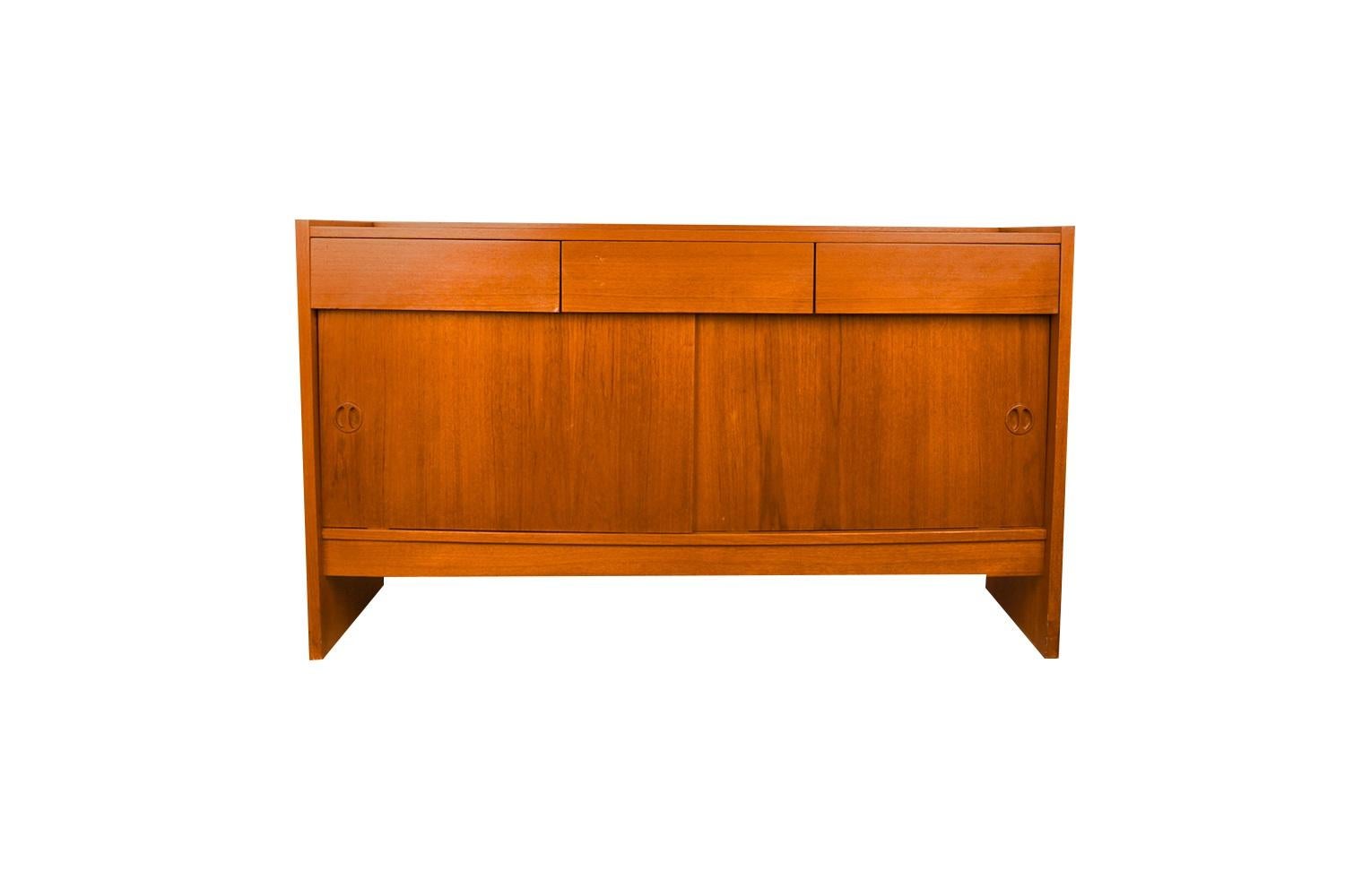 An exceptional teak cabinet/credenza, circa 1970’s, made in Denmark. This absolutely stunning piece features three spacious drawers above a sliding double door cabinet with storage. The cabinet doors are adorned with sculpted pulls, expertly crafted