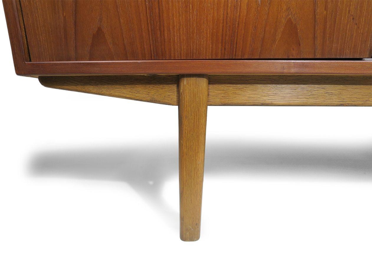 Credenza in teak danese della metà del secolo scorso, caratterizzata da un caratteristico frontale angolare, ante scorrevoli e una serie di tre cassetti centrali con venature abbinate al libro. Le porte scorrevoli si aprono per rivelare un interno
