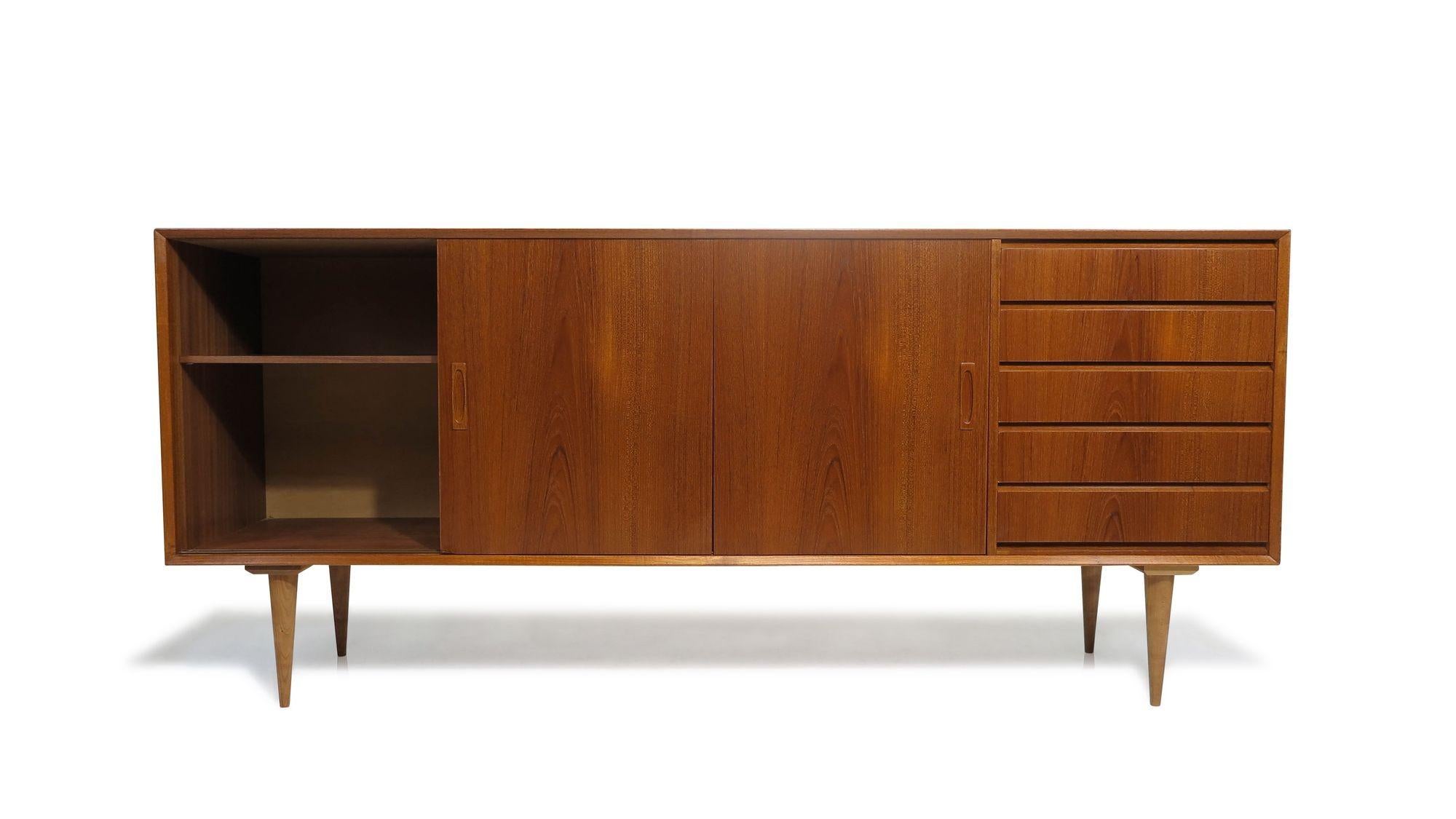 Mid-century teak credenza finely crafted featuring mitered corners, a series of four drawers, and three sliding doors. The sliding doors showcase old-growth teak grain patterns across the front, opening to reveal an interior with adjustable shelves.