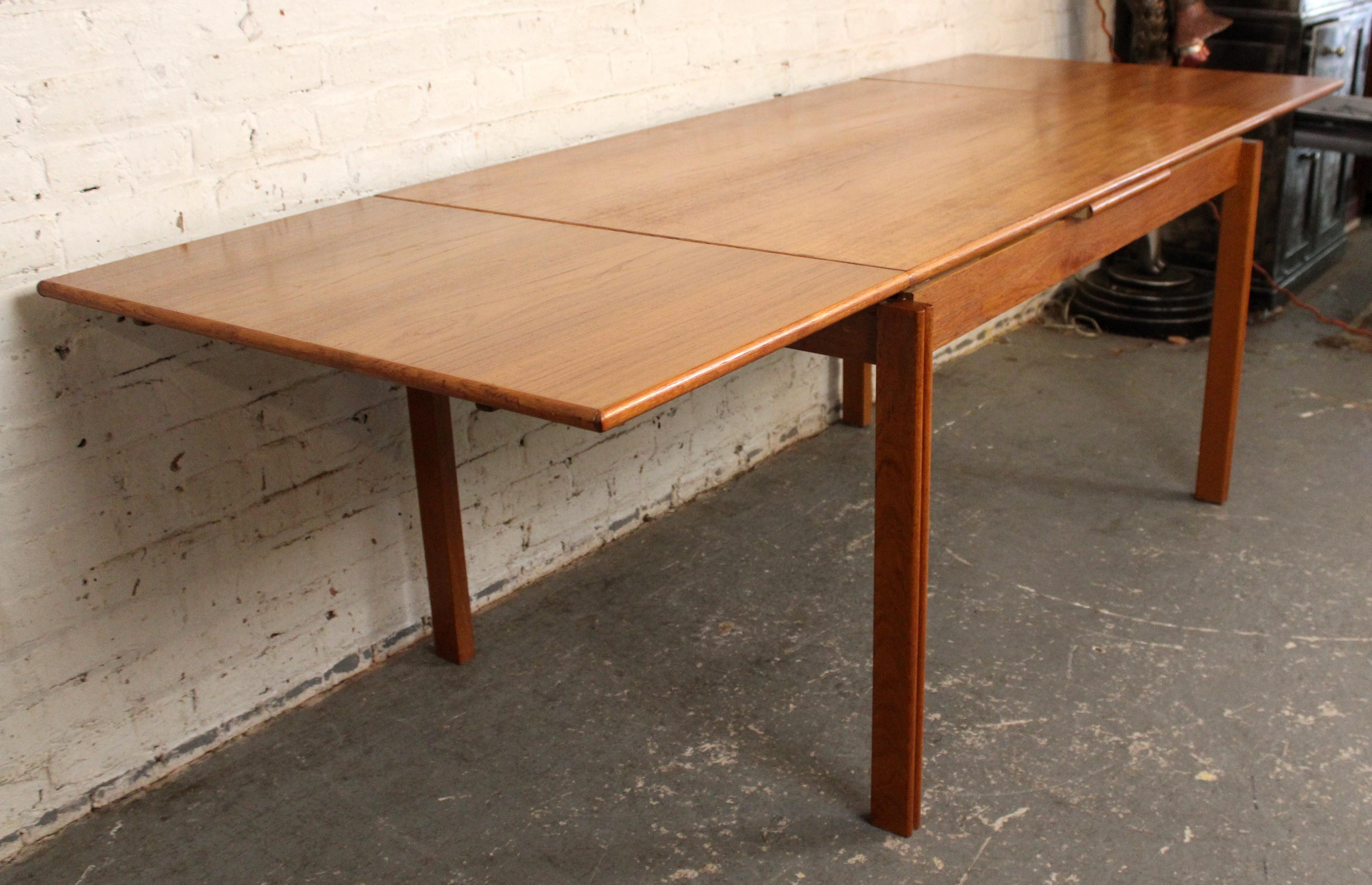 Una mesa de comedor danesa moderna de mediados de siglo, bellamente elaborada, con un rico veteado de madera de teca y un diseño clásico de hojas levadizas. La mesa se extiende sin esfuerzo con dos hojas extraíbles ocultas bajo el tablero,