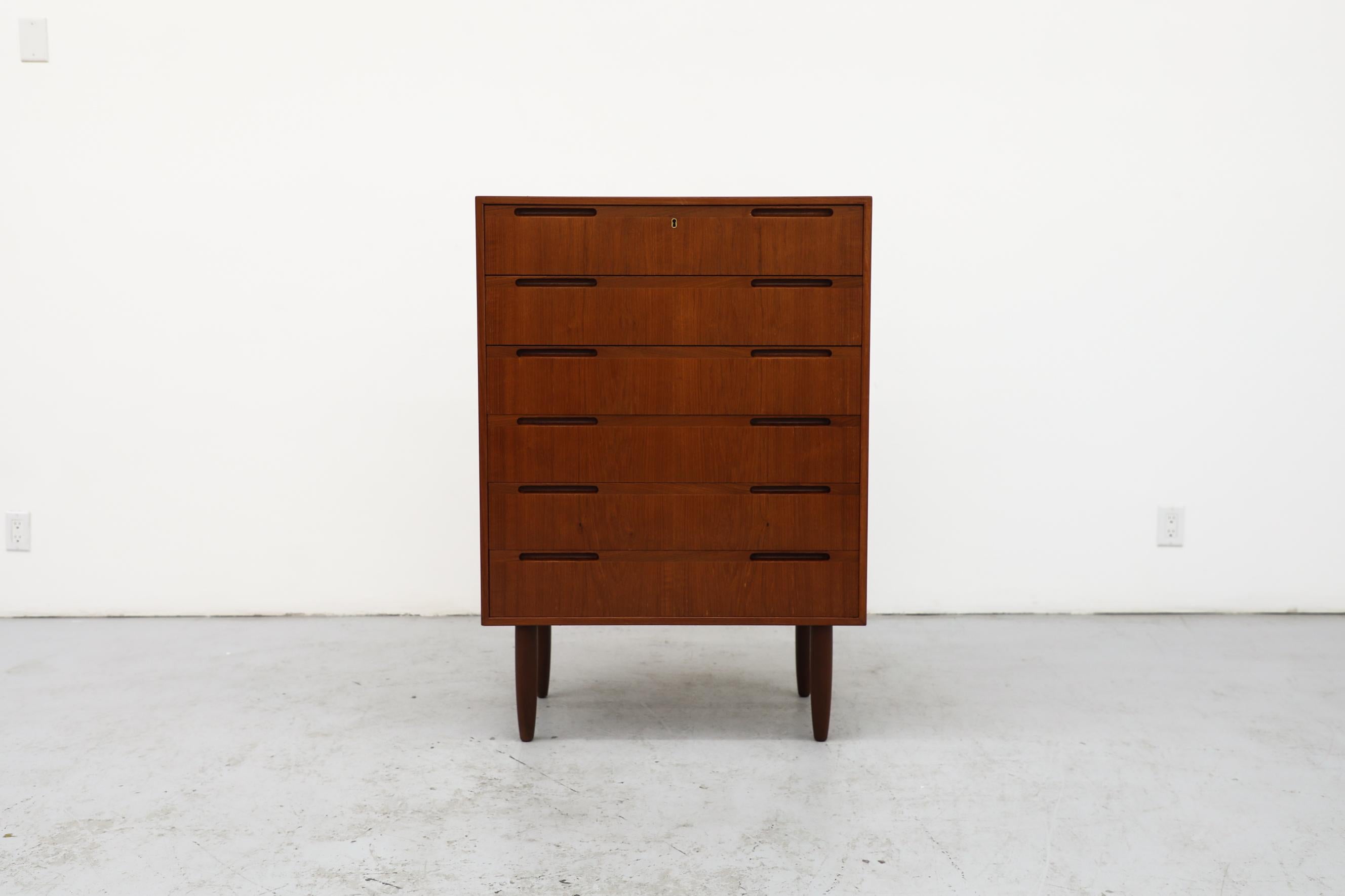This Mid-Century Danish teak tall standing dresser has 6 drawers, inset carved pulls and tapered legs. It has been lightly refinished with some remaining wear, consistent with its age and use.