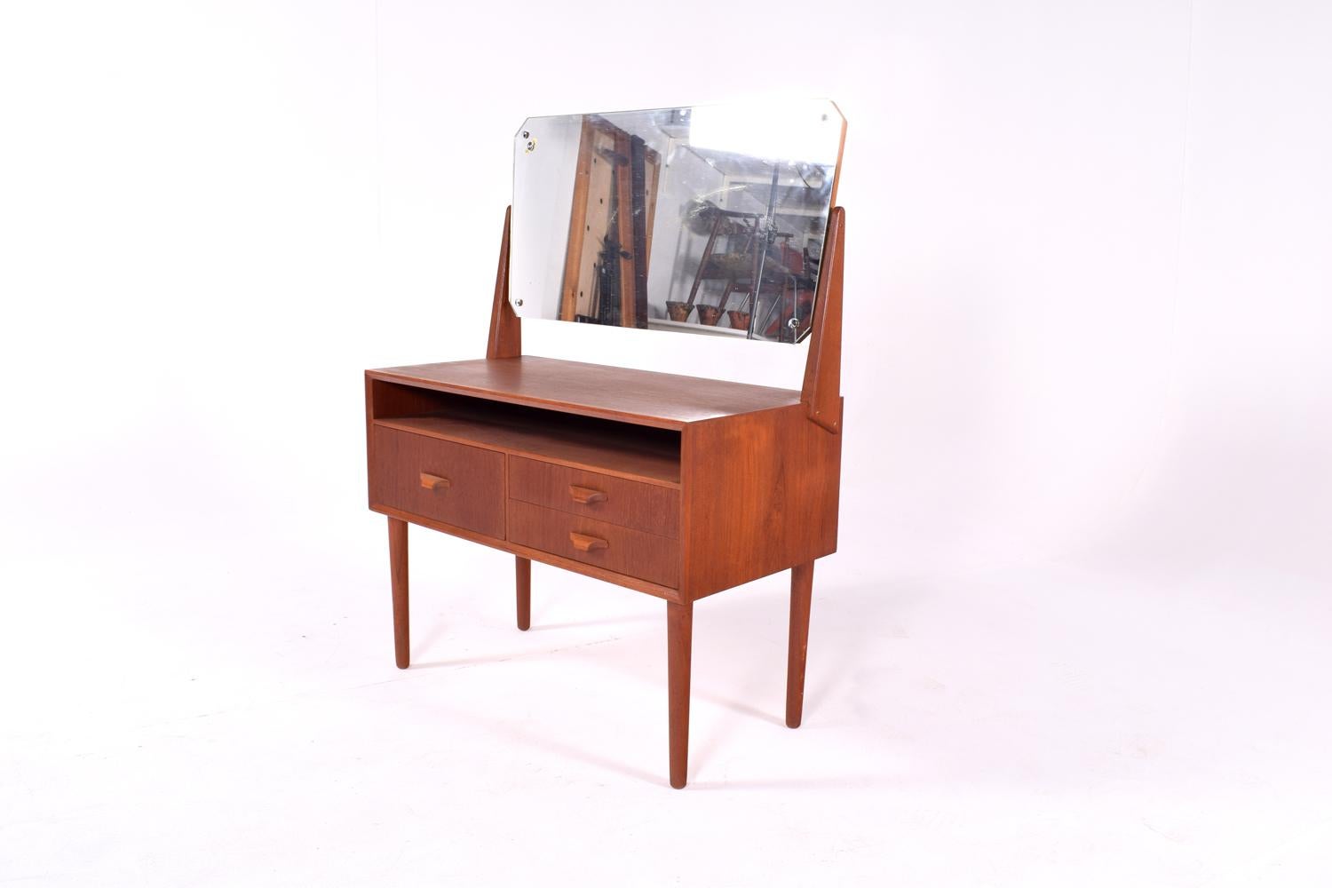 Danish teak dressing table with large mirror. The dressing table was made in the 1960s and has a nice elegant and slim design. The large mirror is tiltable. The dressing table has 3 drawers and a shelf.